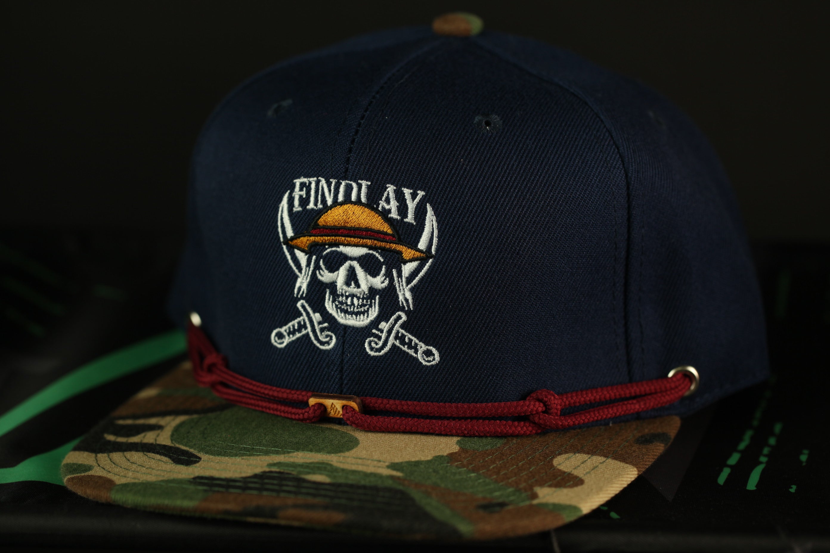 A navy blue baseball cap with a camouflage pattern and a skull and crossbones design on the front.