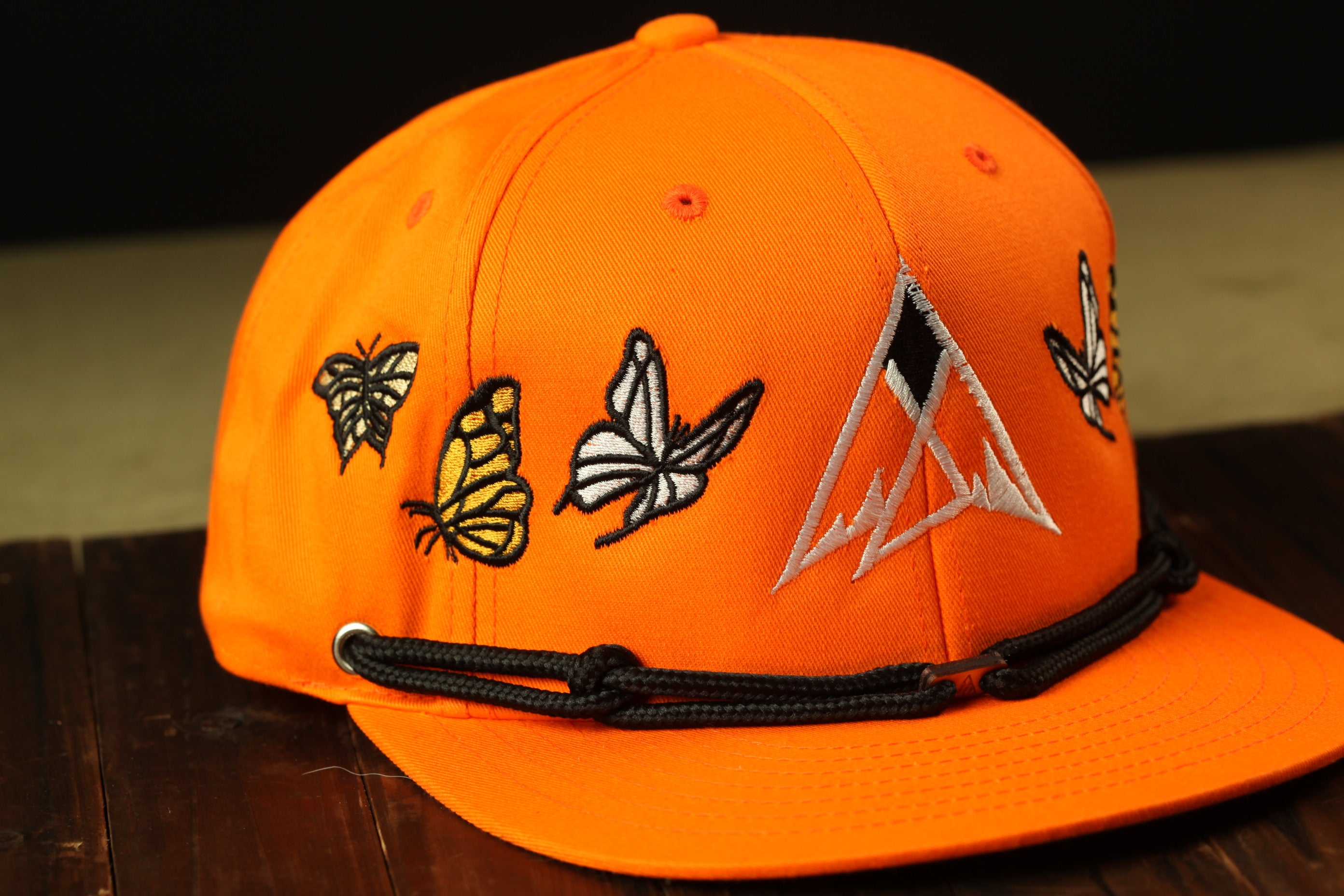 An orange baseball cap with a black band and embroidered butterflies on the front.