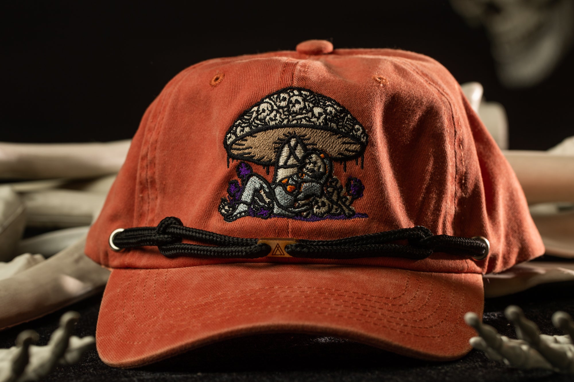 An orange baseball cap with a mushroom design on it, resting on a surface with some bones or skeletal structures in the background.