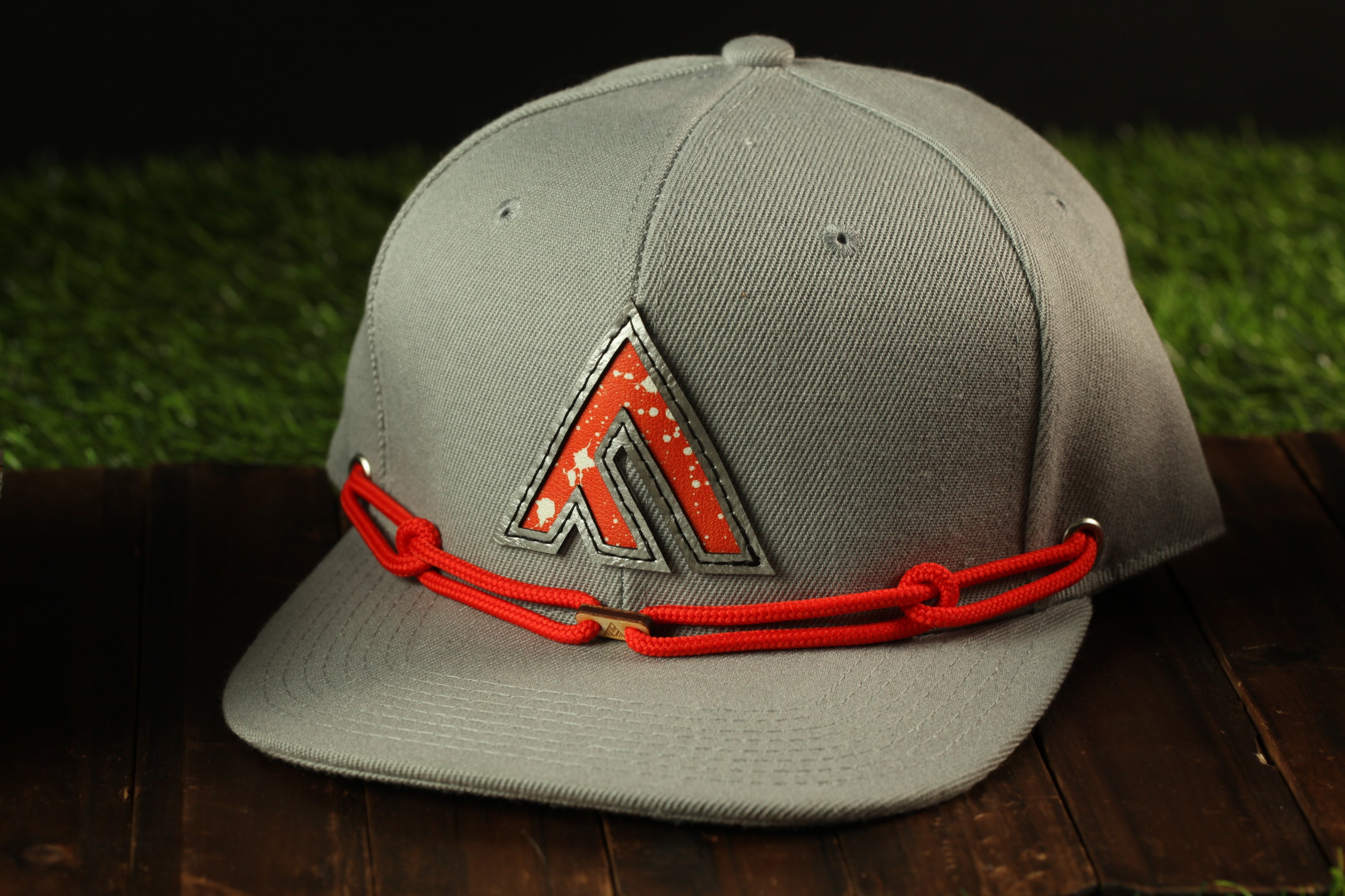 A gray baseball cap with a red rope and a logo on the front, placed on a wooden surface.