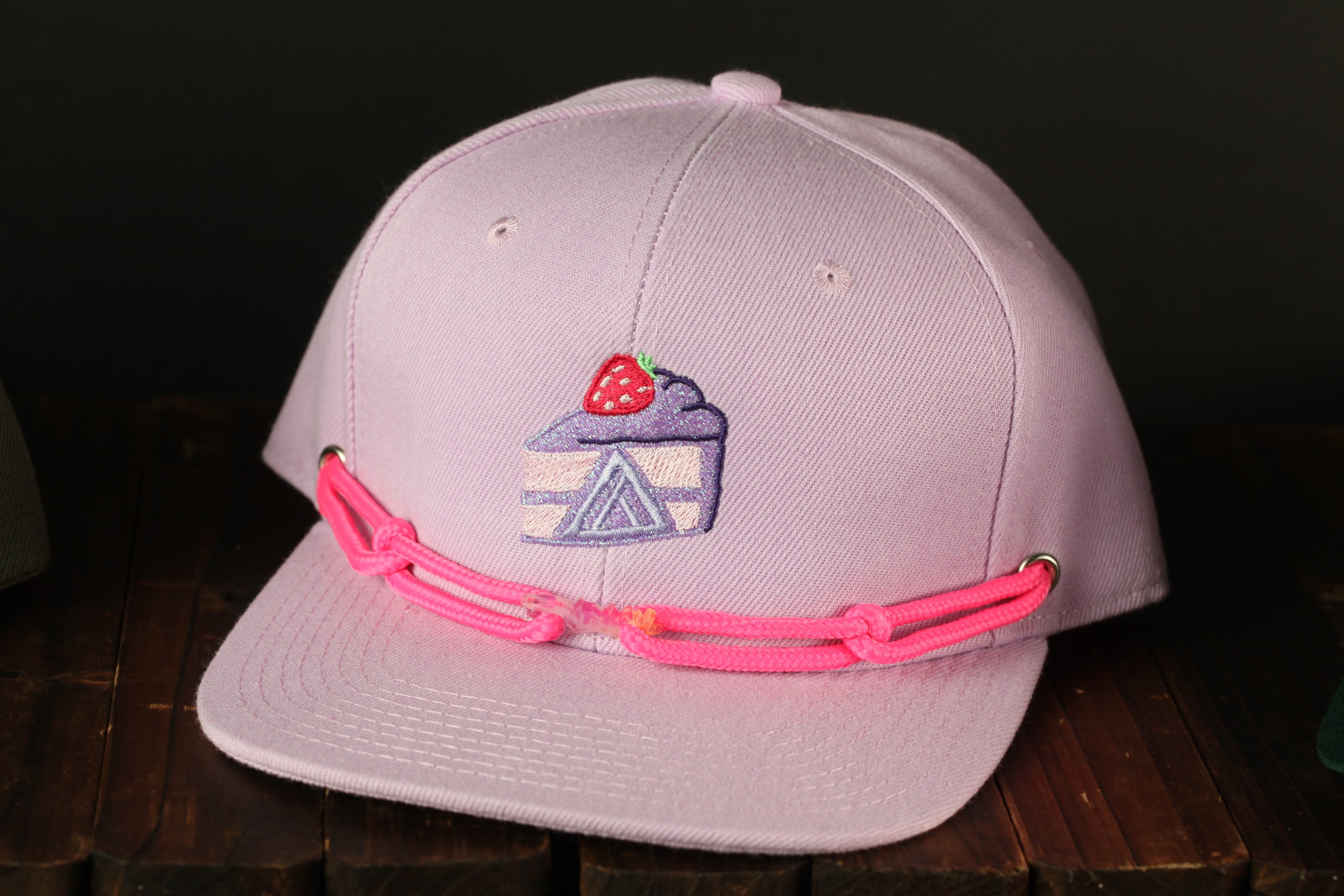 A pink baseball cap with a strawberry design on the front, sitting on a wooden surface.