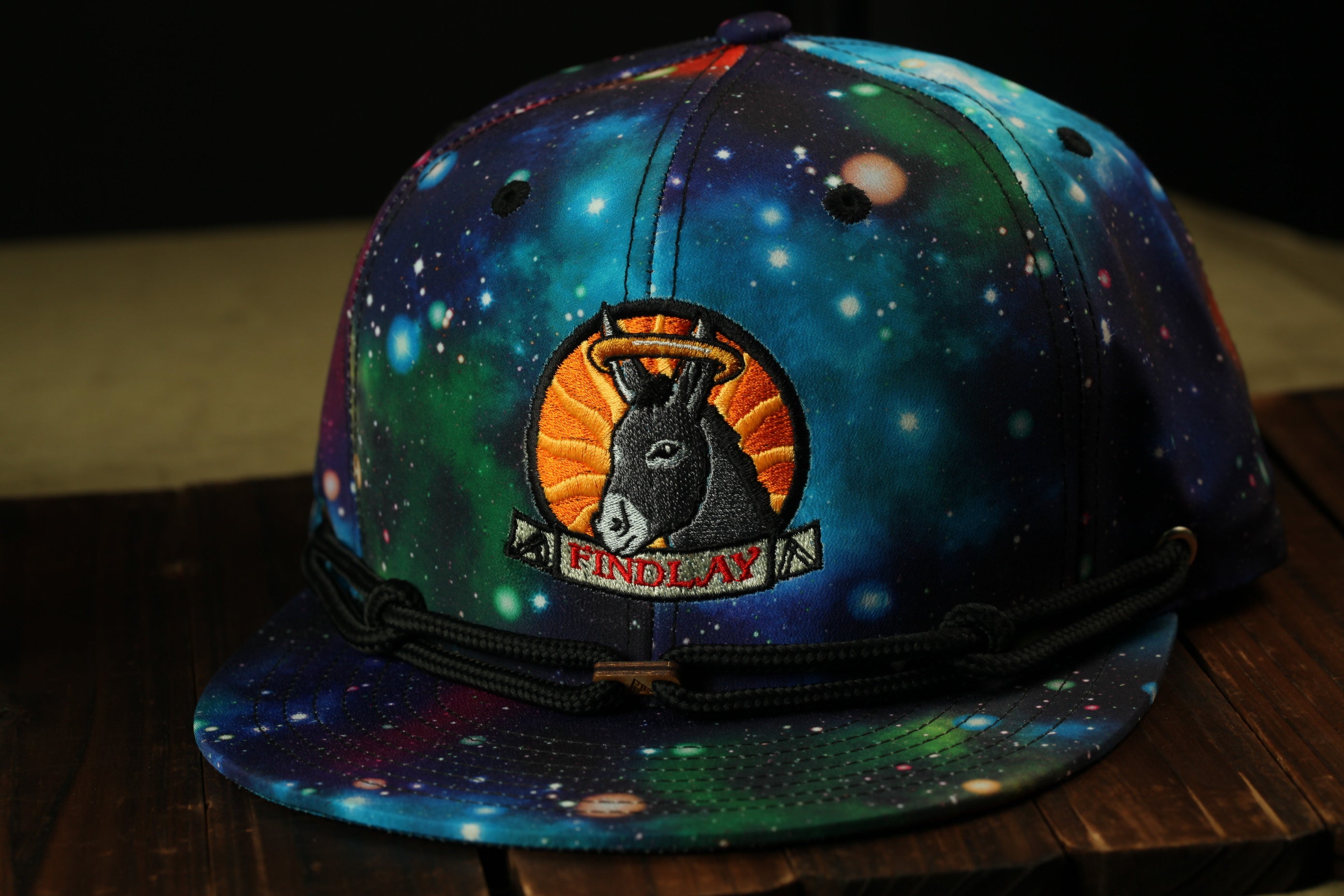 A colorful baseball cap with a space-themed design, featuring a donkey-like creature and the word "FINDlay" on the front.