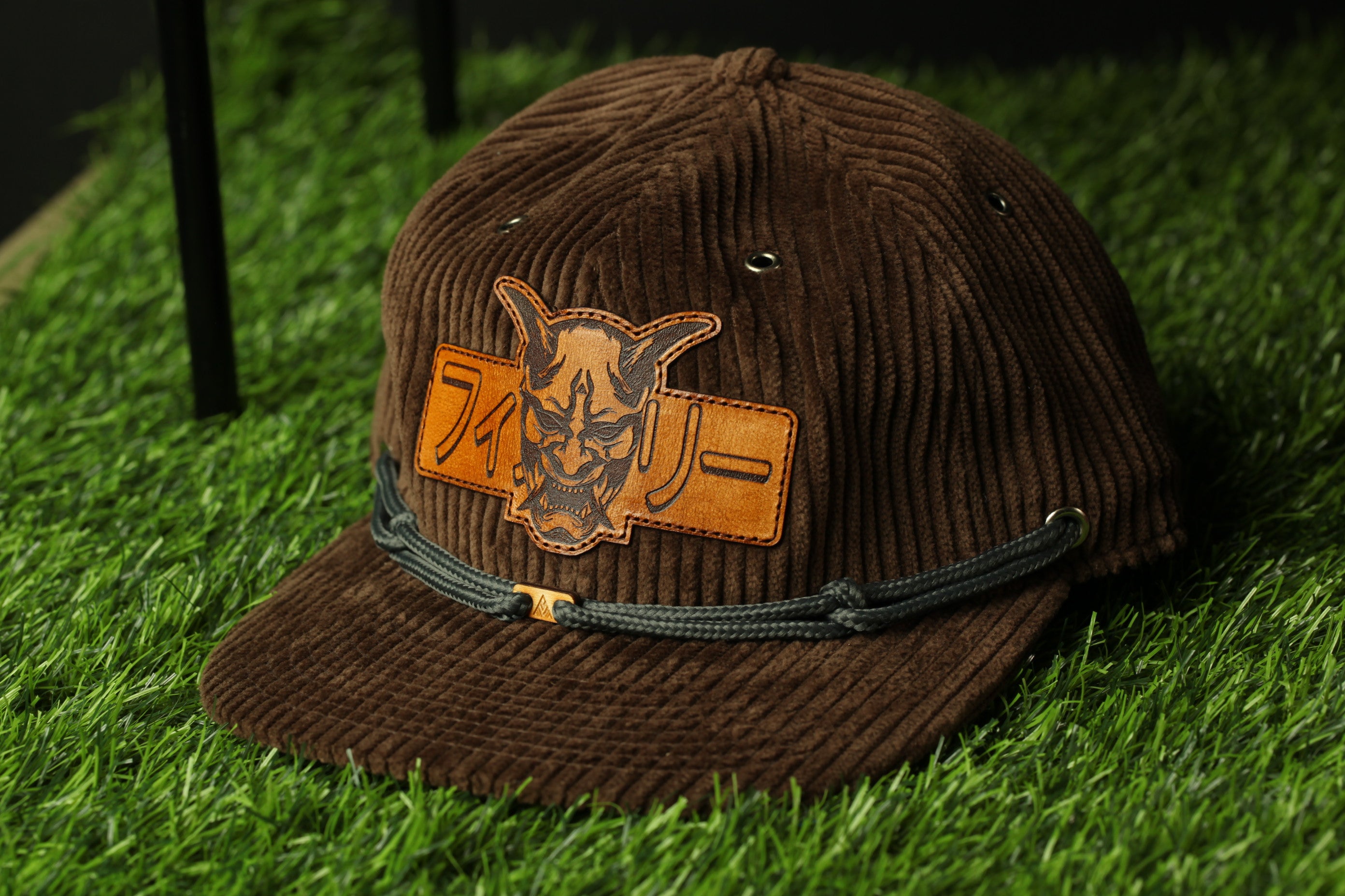 A brown baseball cap with a distinctive orange and black design on the front, resting on a grassy surface.
