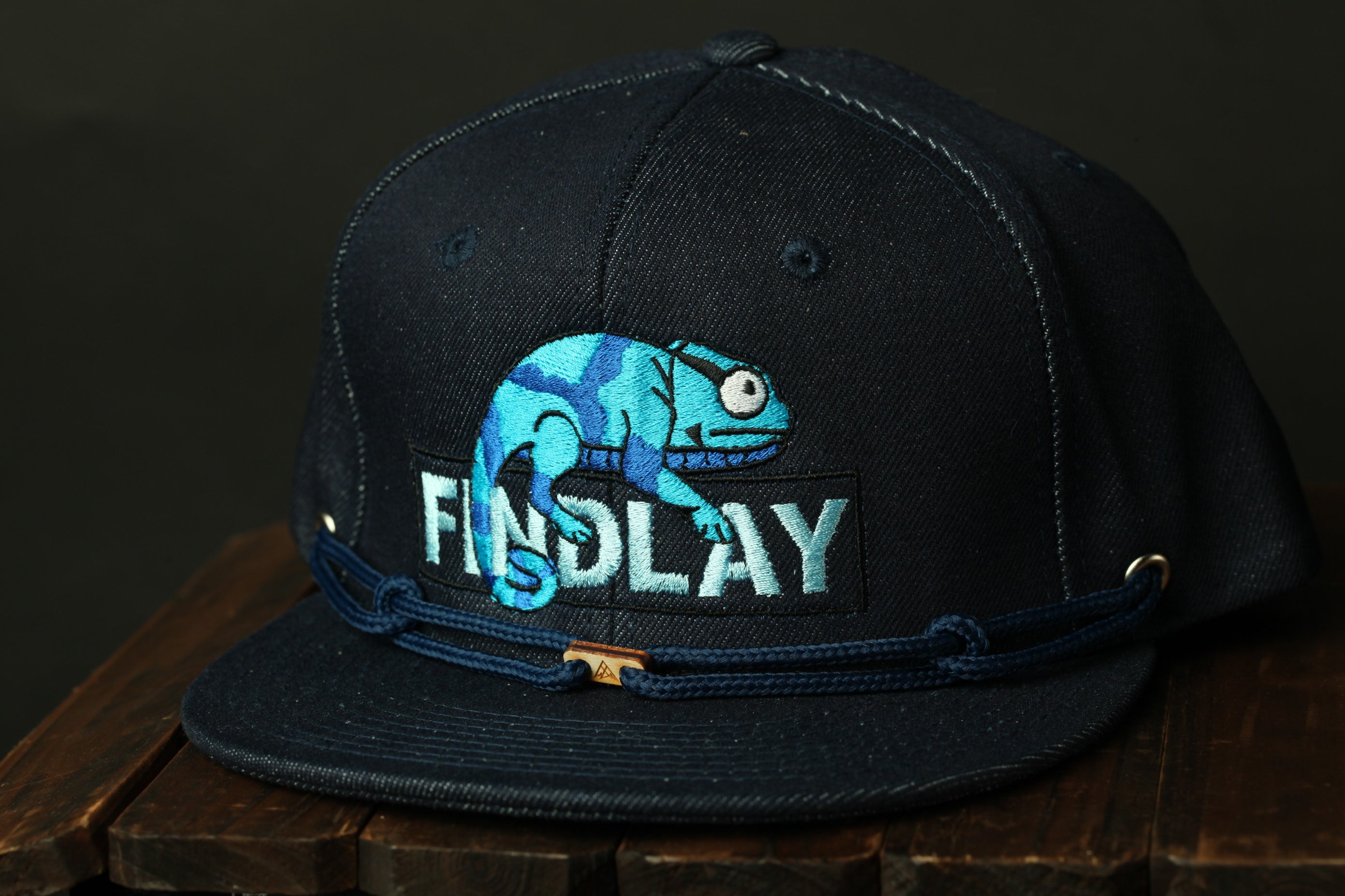 A black baseball cap with a blue chameleon design and the word "FINDlay" printed on it.