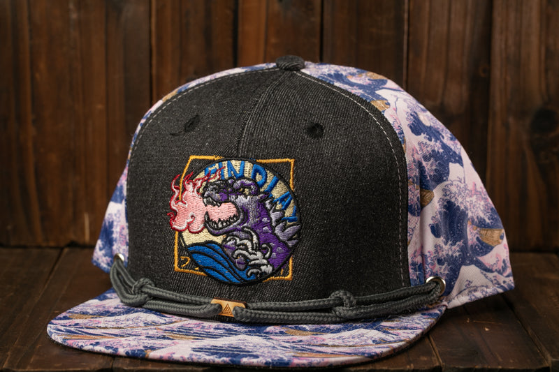 A black baseball cap with a colorful graphic and a wave pattern on the brim, placed on a wooden surface.