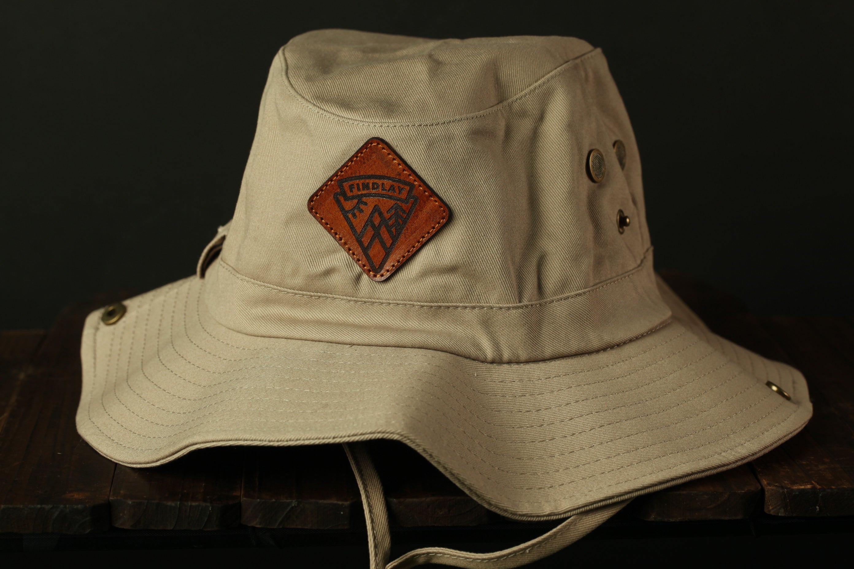 A beige bucket hat with a leather patch on the front, placed on a wooden surface.