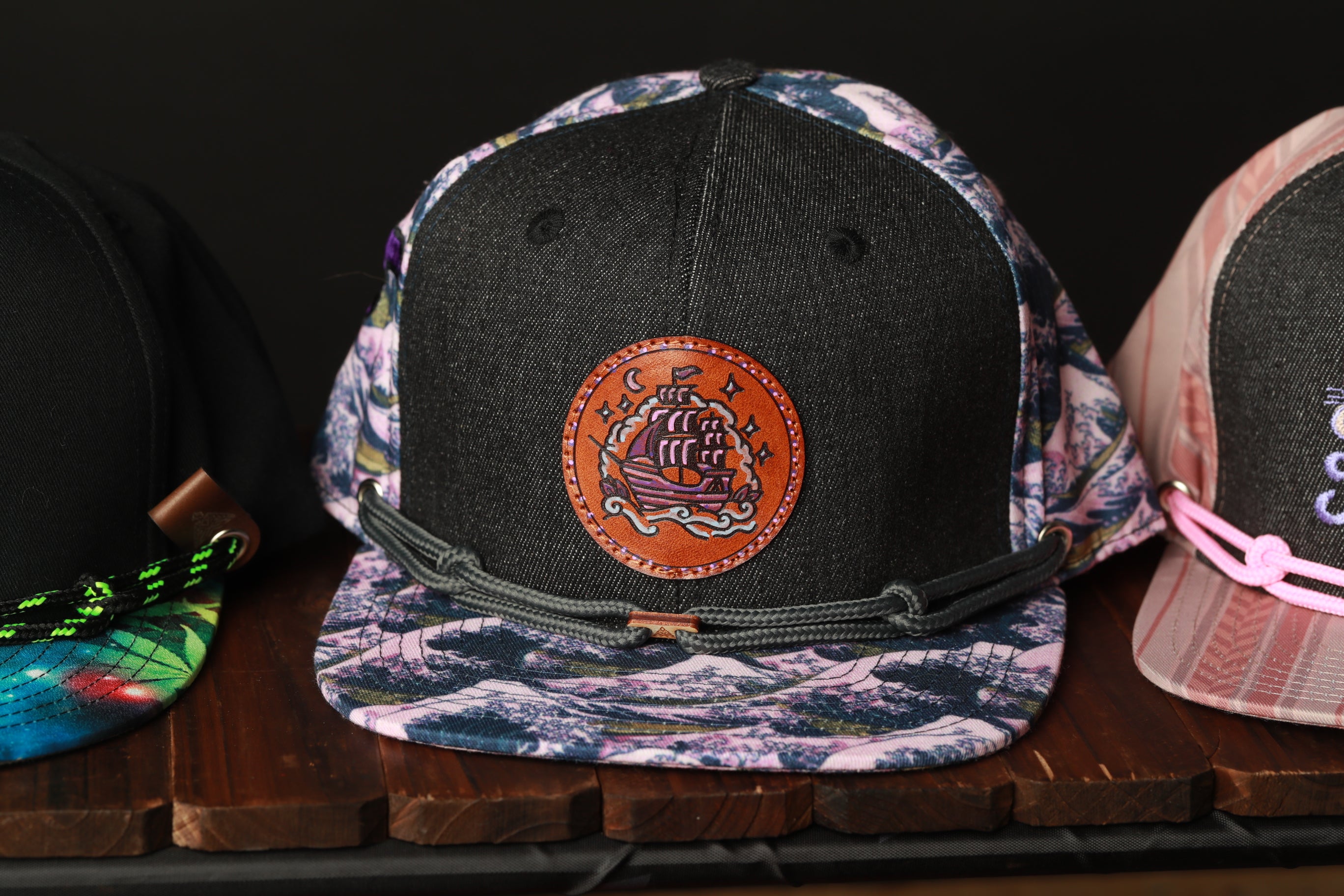 A close-up view of three colorful baseball caps on a wooden surface, with one featuring a unique circular design.