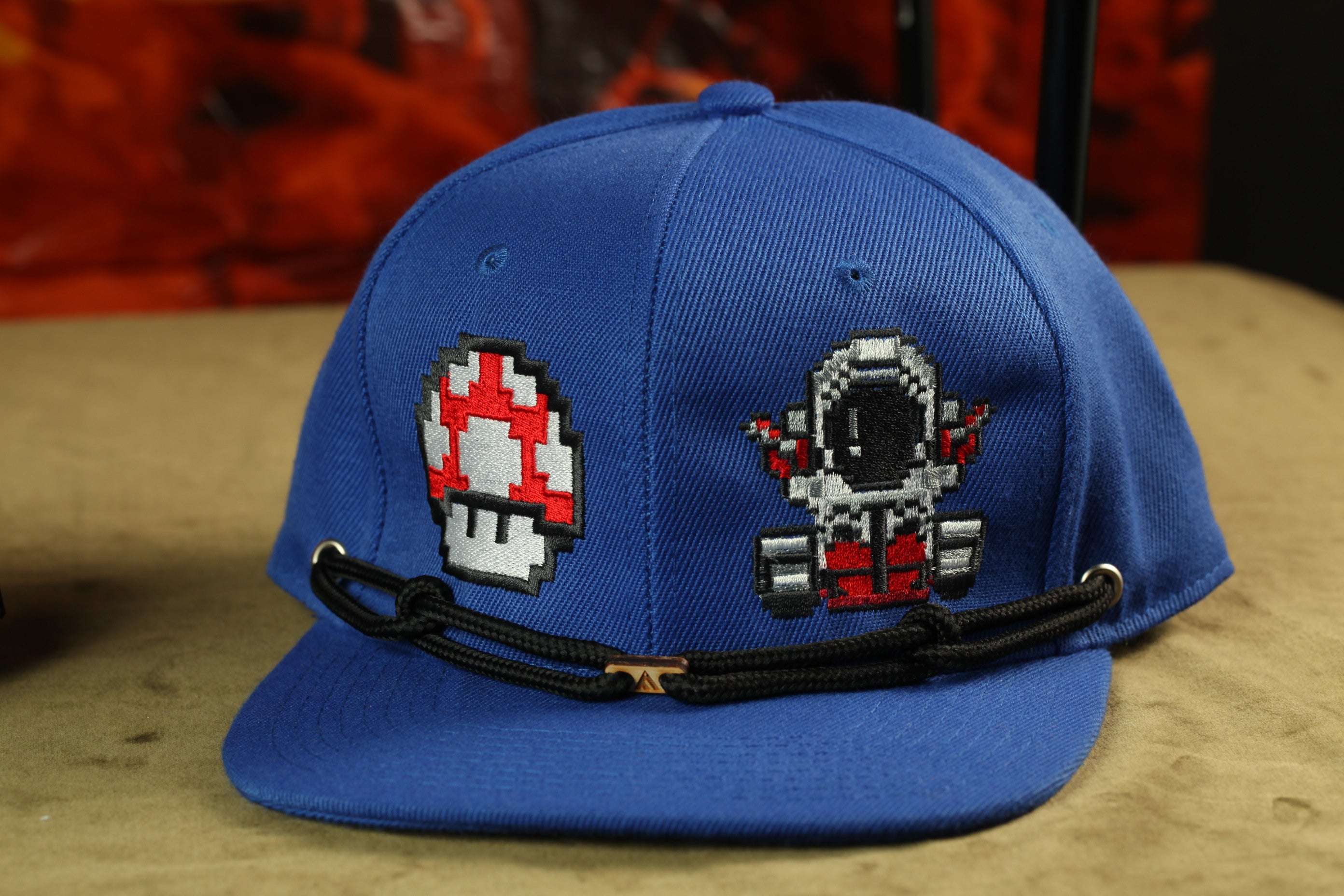 A blue baseball cap with two pixelated character designs on the front.