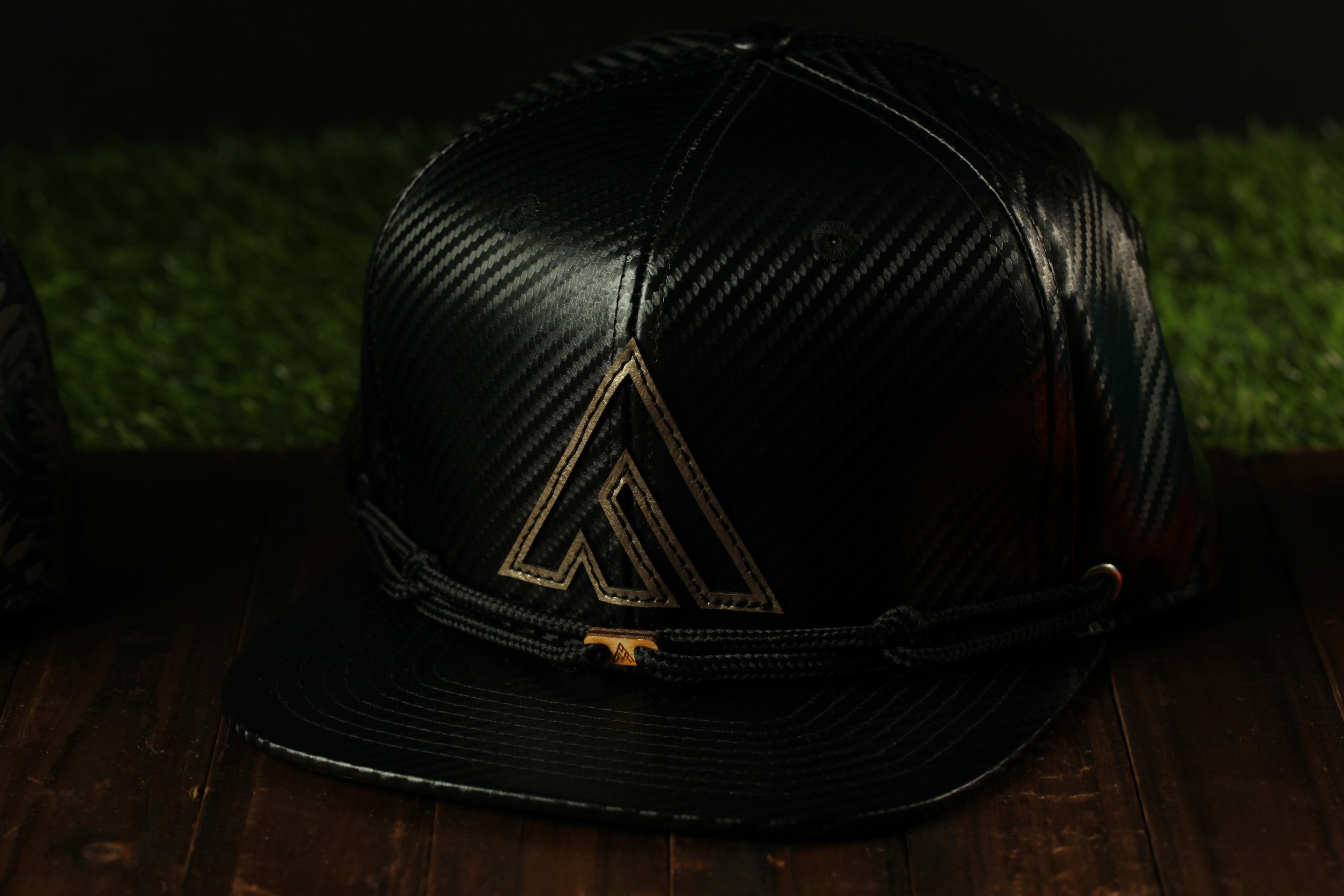 A black baseball cap with a gold logo on the front, placed on a wooden surface.
