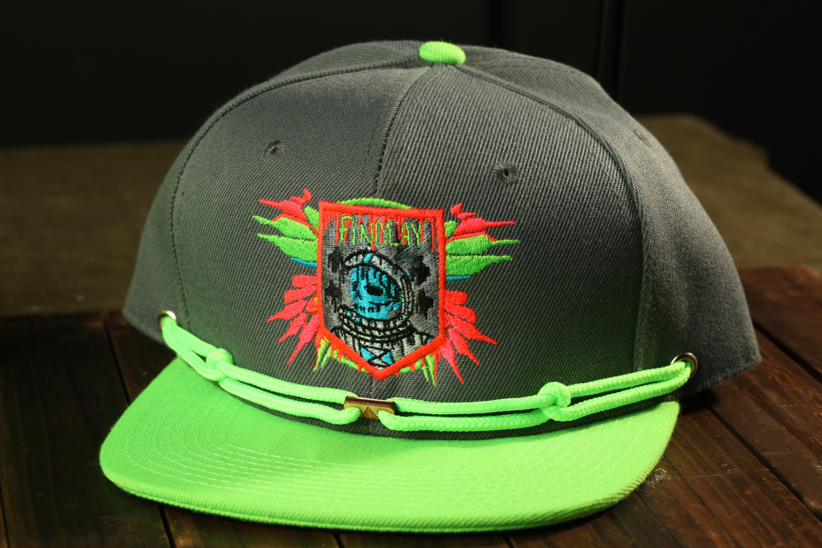 A dark green baseball cap with a neon green brim and a colorful graphic design on the front.