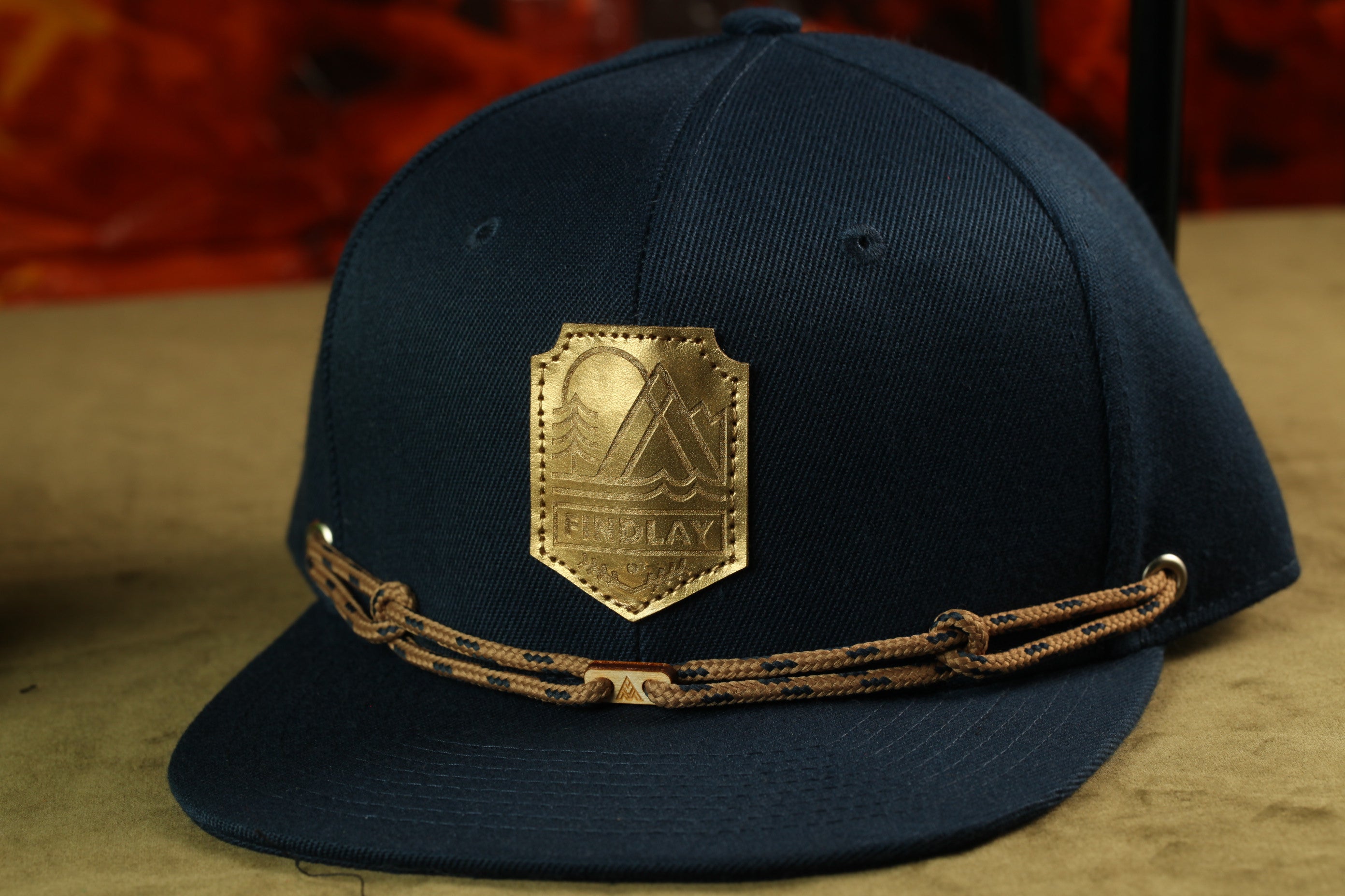 A navy blue baseball cap with a gold patch and a brown braided strap.