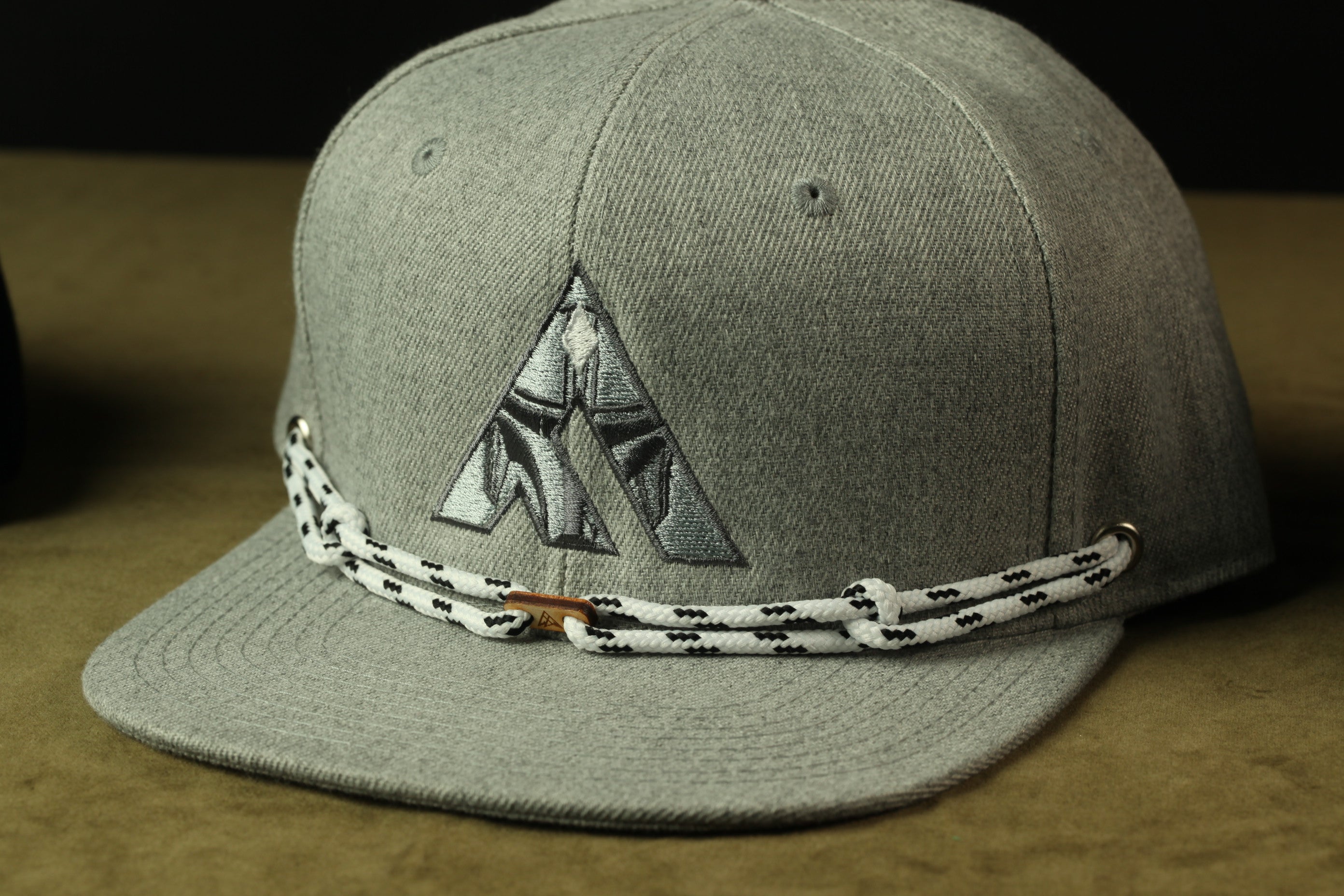 A gray baseball cap with a black and white braided strap and a logo on the front.
