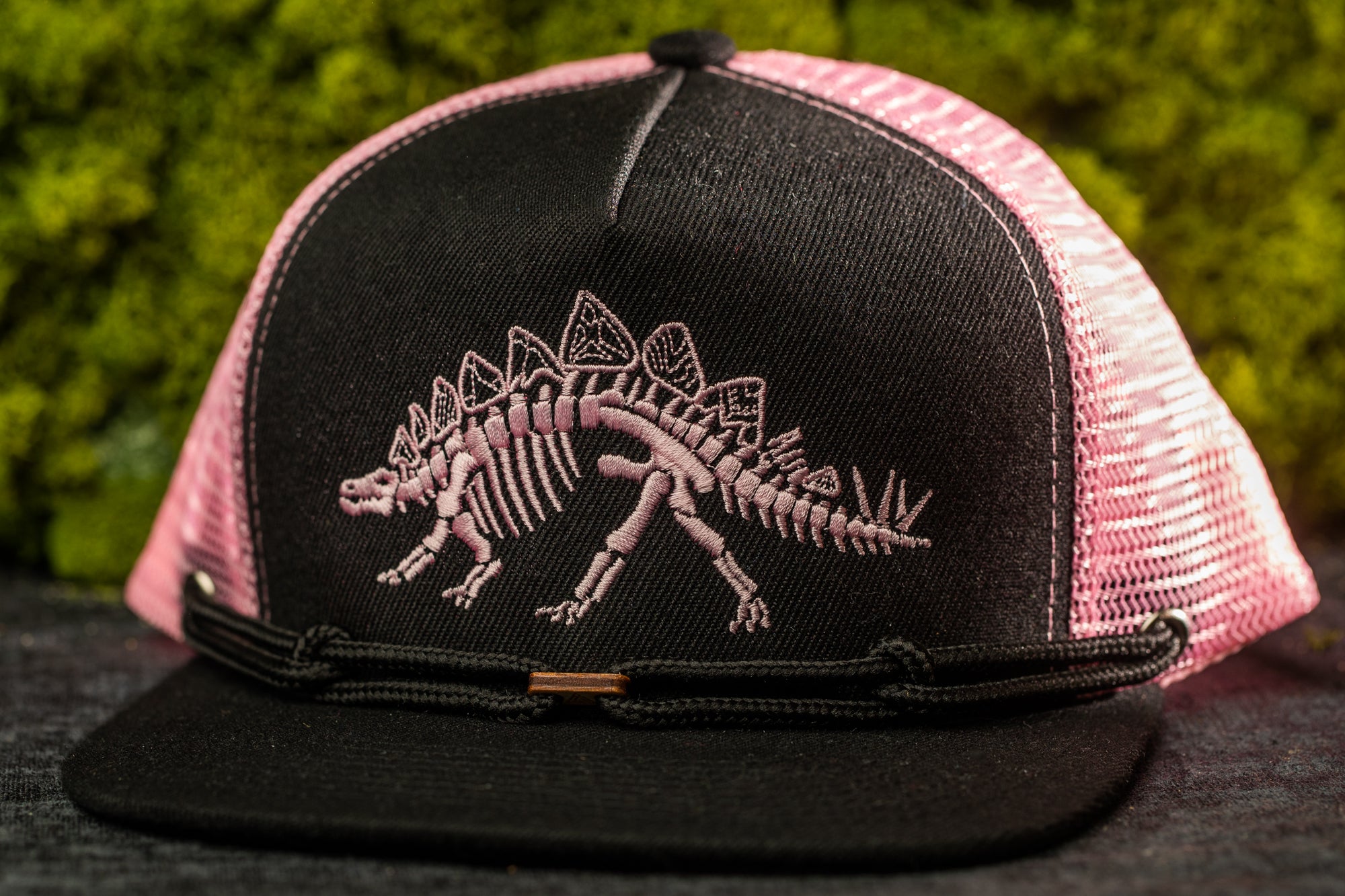 A black and pink baseball cap with a dinosaur skeleton embroidered on it.