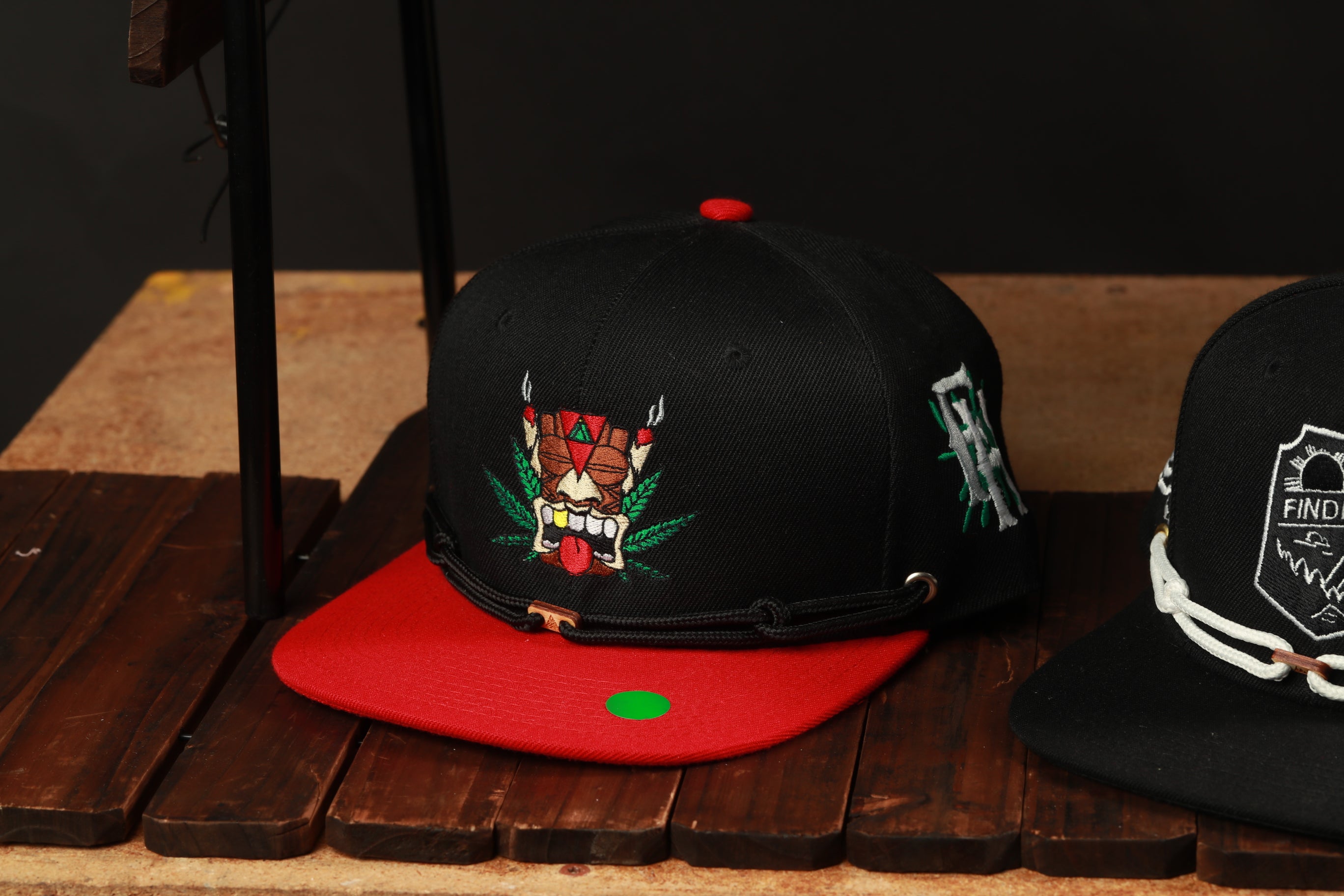 A black baseball cap with a red brim and a graphic design on the front, placed on a wooden surface.