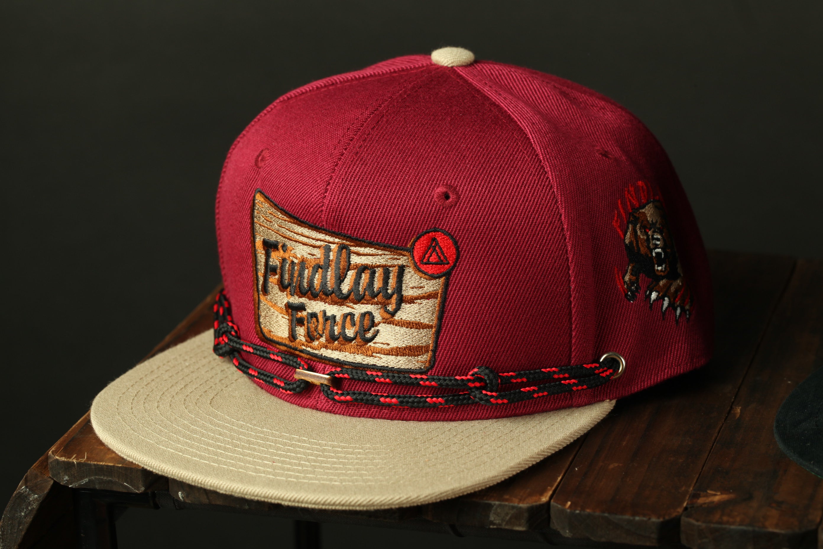 A maroon baseball cap with a red and black braided strap, featuring a patch with the text "Fondly Force" and a graphic of a bear.