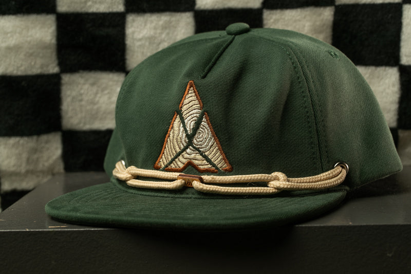 A green baseball cap with a white and orange logo on the front, sitting on a black surface against a checkered background.