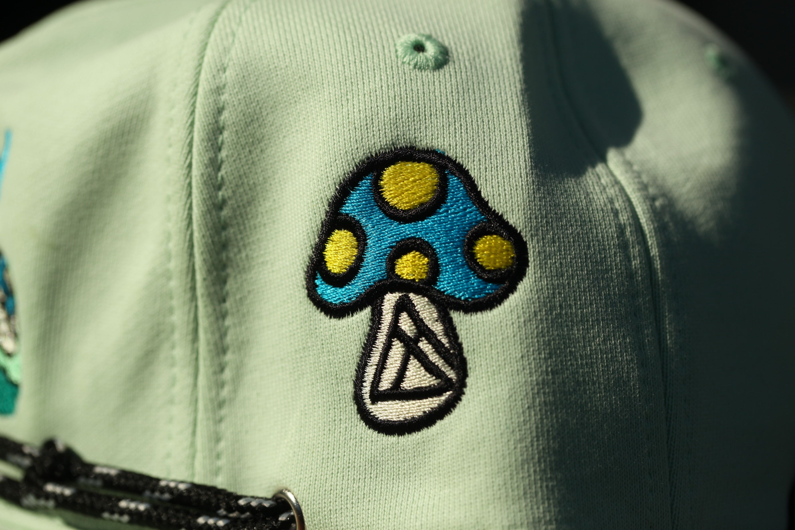 A close-up view of a green baseball cap with a blue and yellow mushroom embroidered on it.