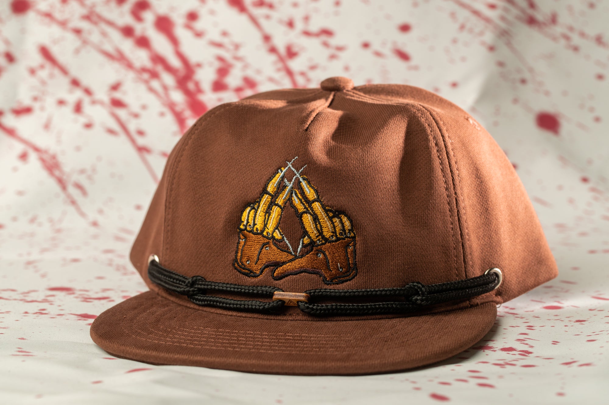 A brown baseball cap with a graphic design on the front, featuring a pair of crossed fingers.