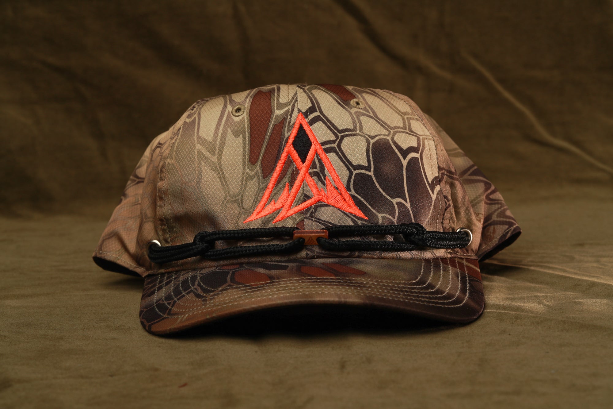 A camouflage-patterned baseball cap with a red triangle logo on the front, resting on a brown surface.