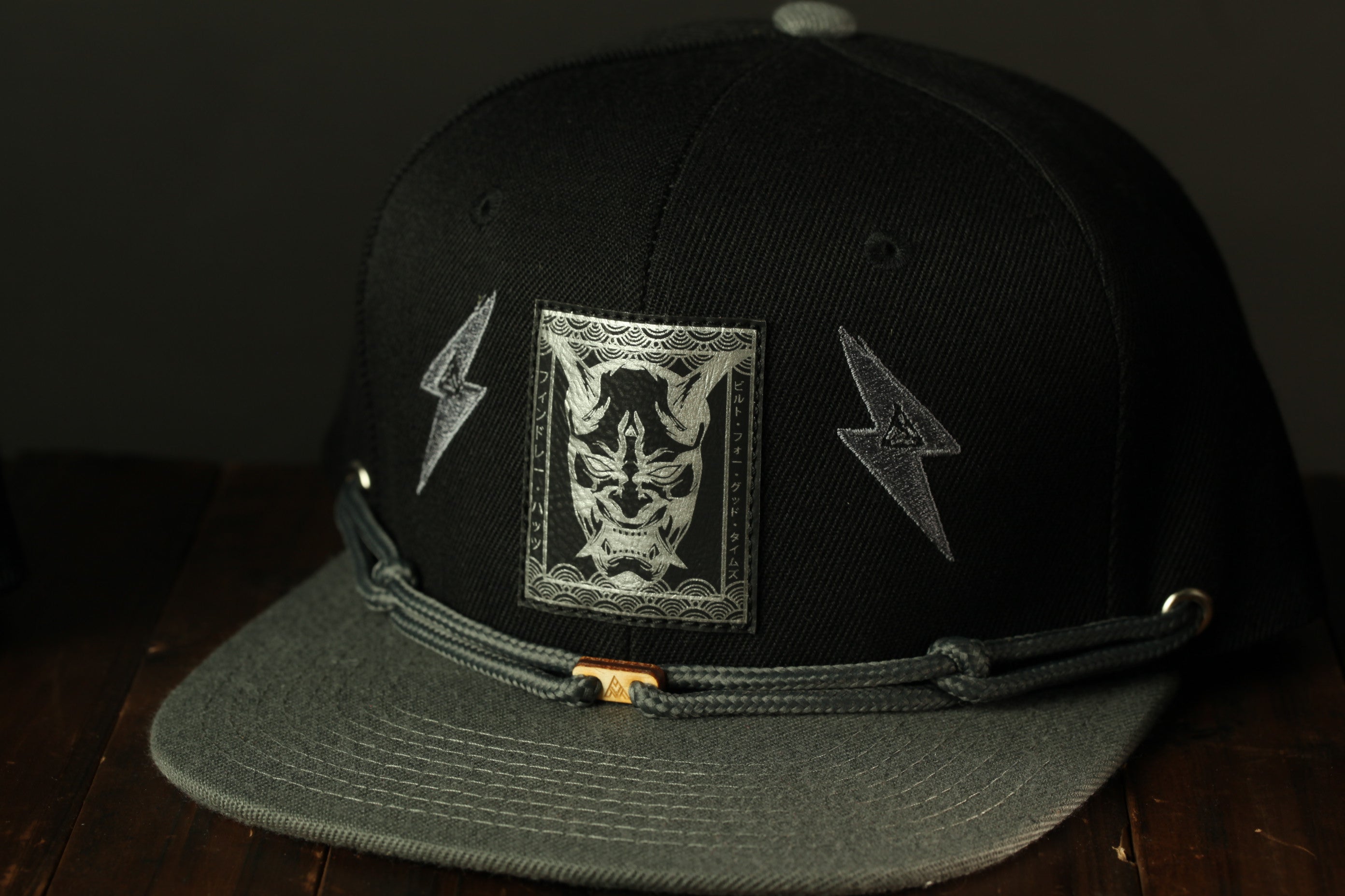 A black baseball cap with a graphic design on the front, including a mask and lightning bolts.