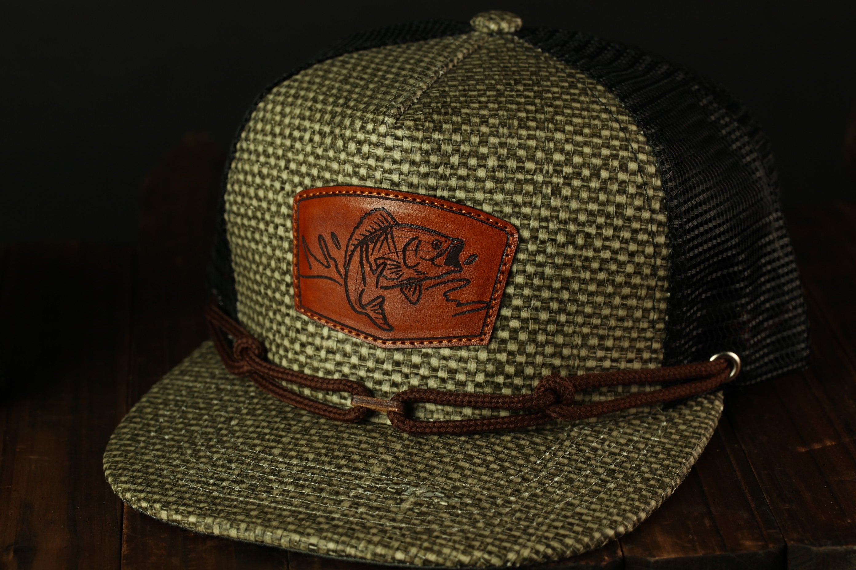 A green and black baseball cap with a brown leather patch featuring a fish design.
