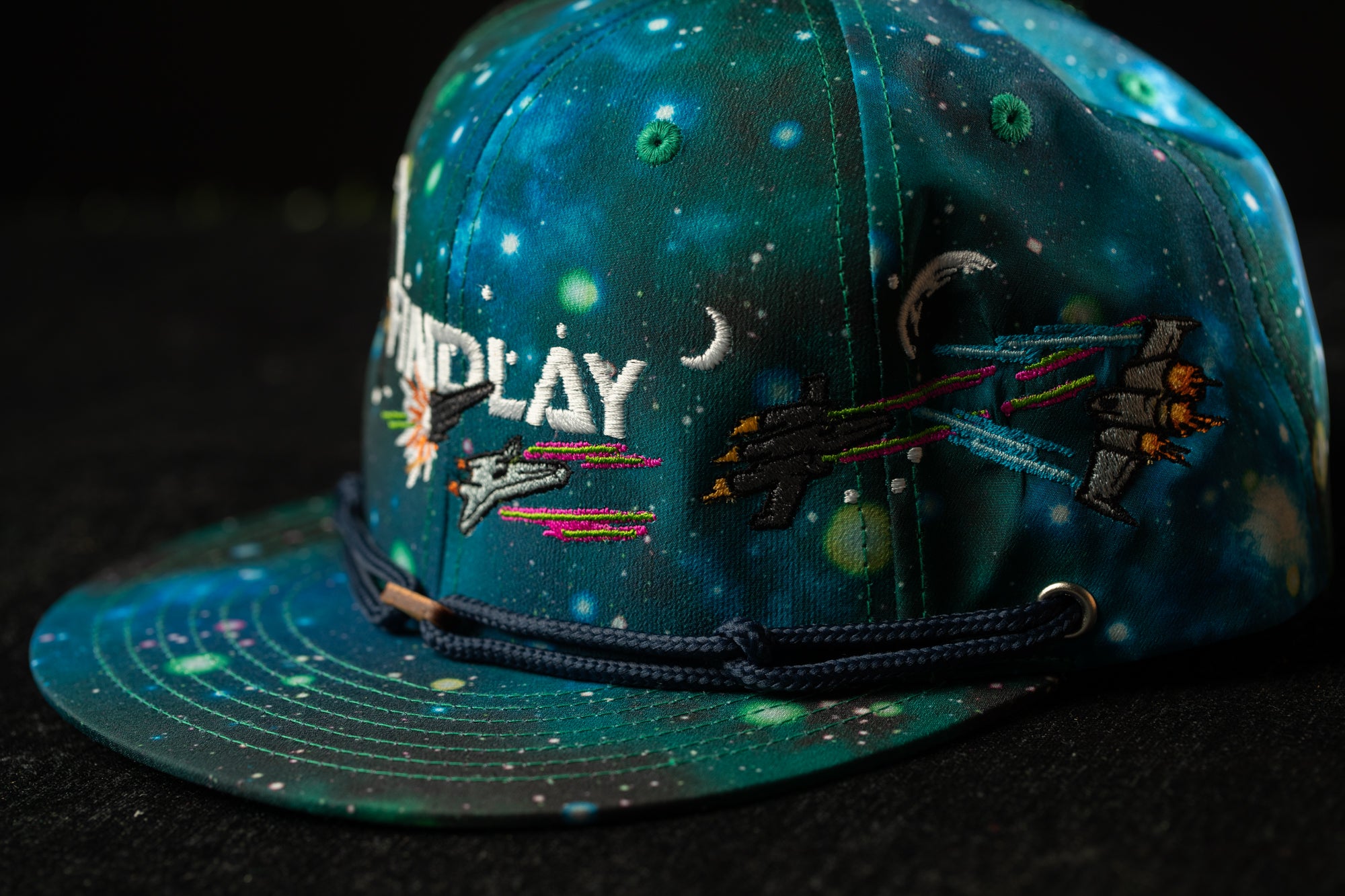 A colorful baseball cap with a space-themed design, featuring a crescent moon, stars, and a spaceship embroidered on the front.