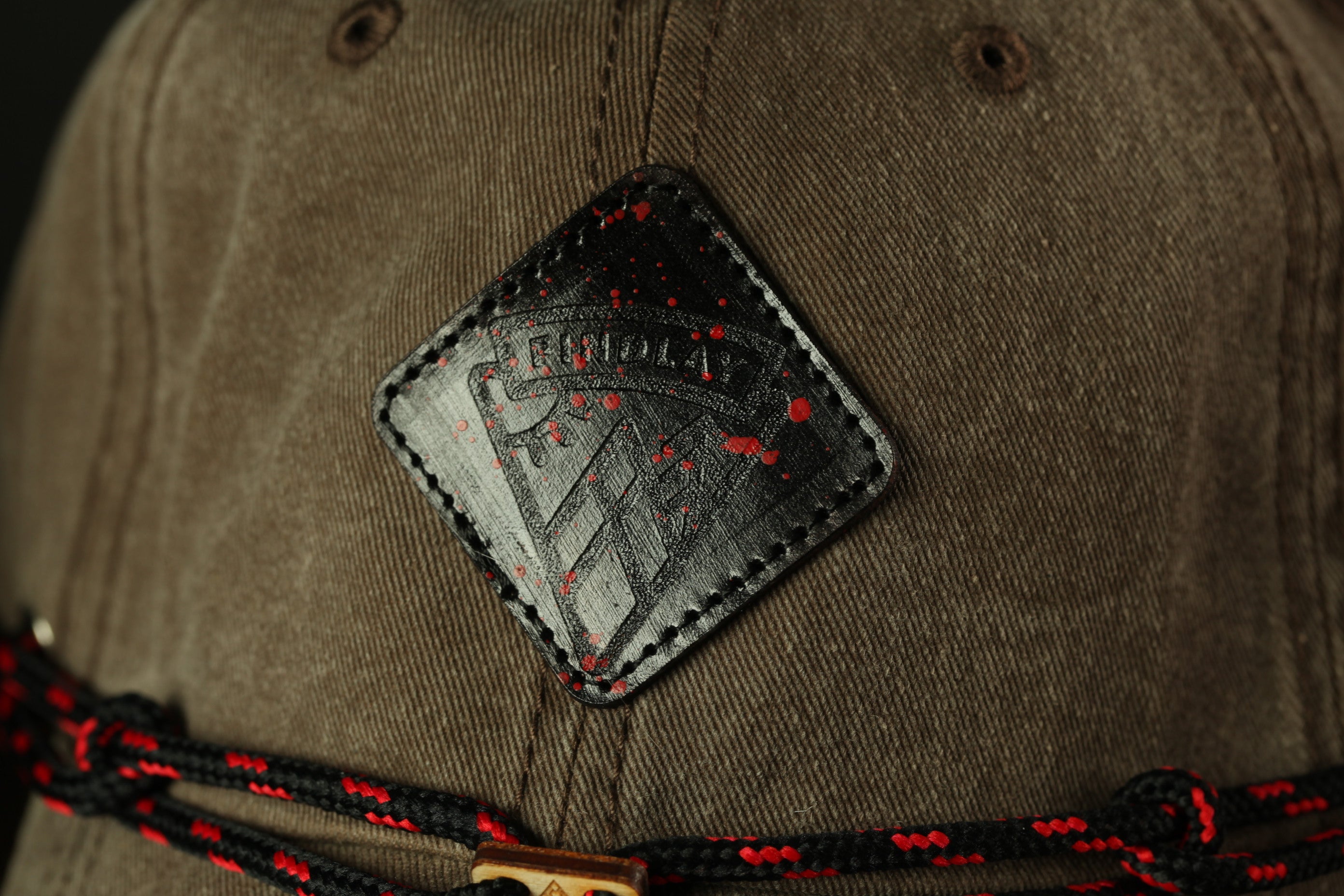 A close-up view of a brown baseball cap with a black and red logo on the front.
