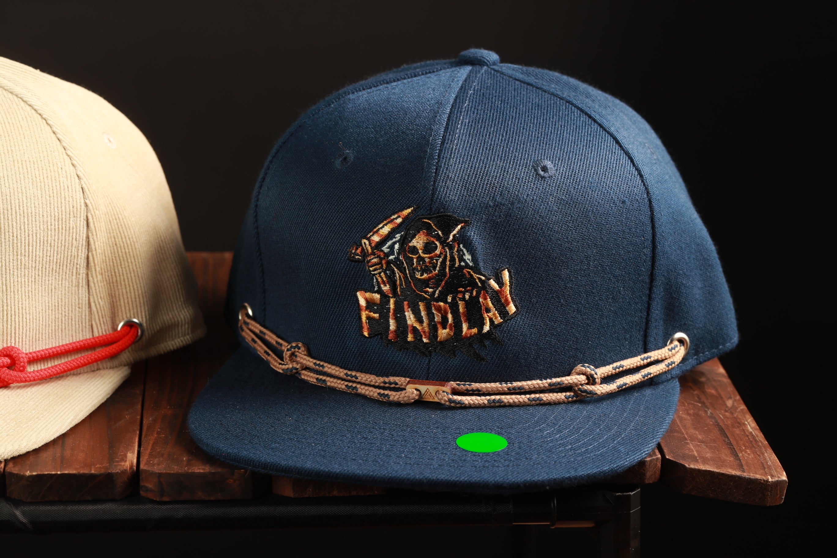 A navy blue baseball cap with a pirate logo and a red string is displayed on a wooden surface.