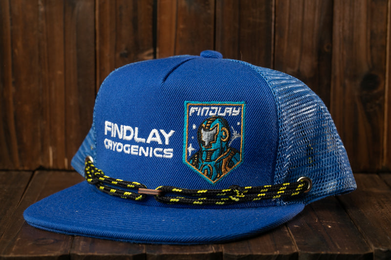 A blue baseball cap with the text "Findlay Cryogenics" printed on it, along with a shield-shaped logo featuring a robot or cyborg-like figure.