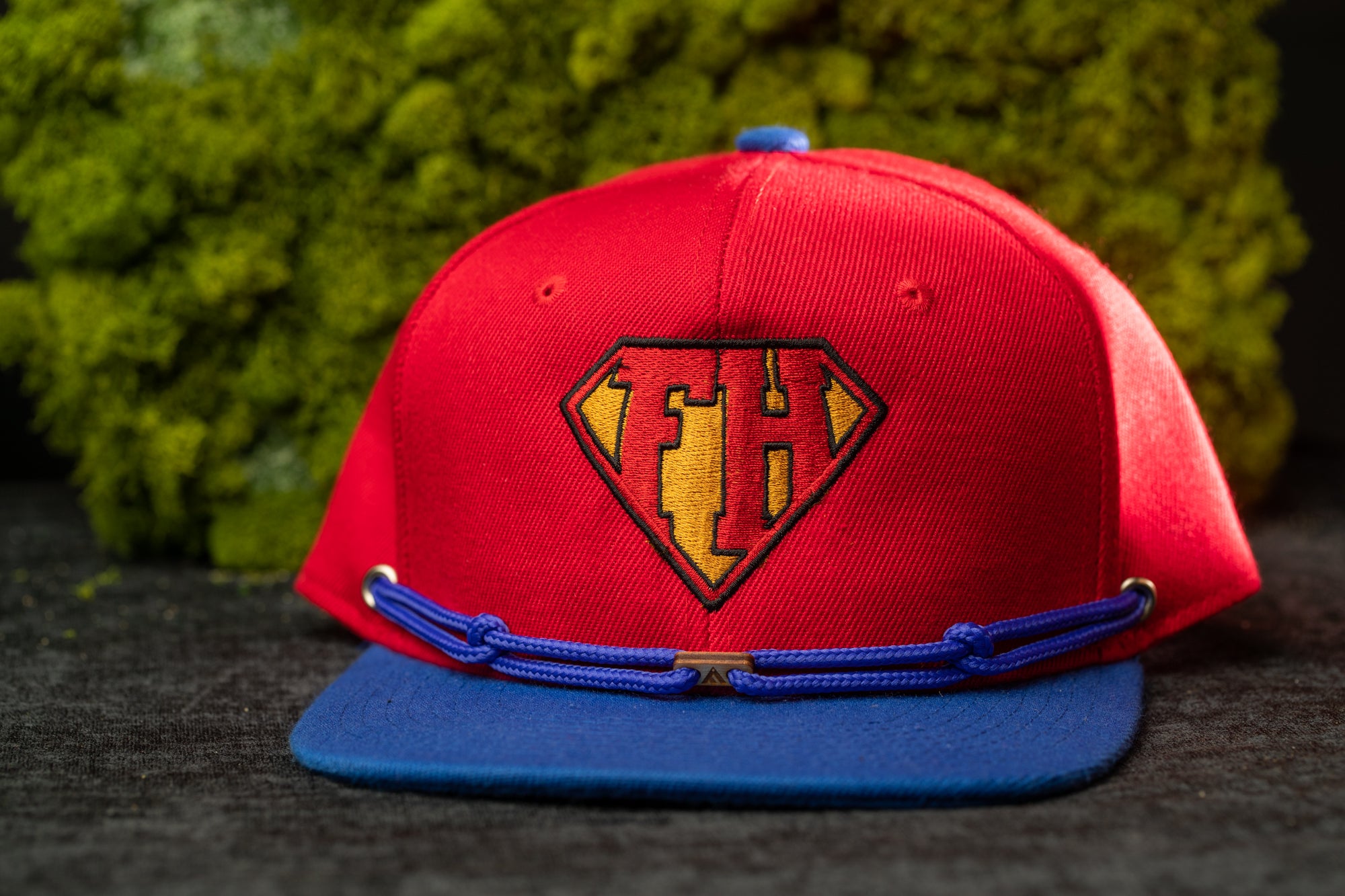 A red baseball cap with a blue brim and a blue band around the front, featuring a logo on the front.