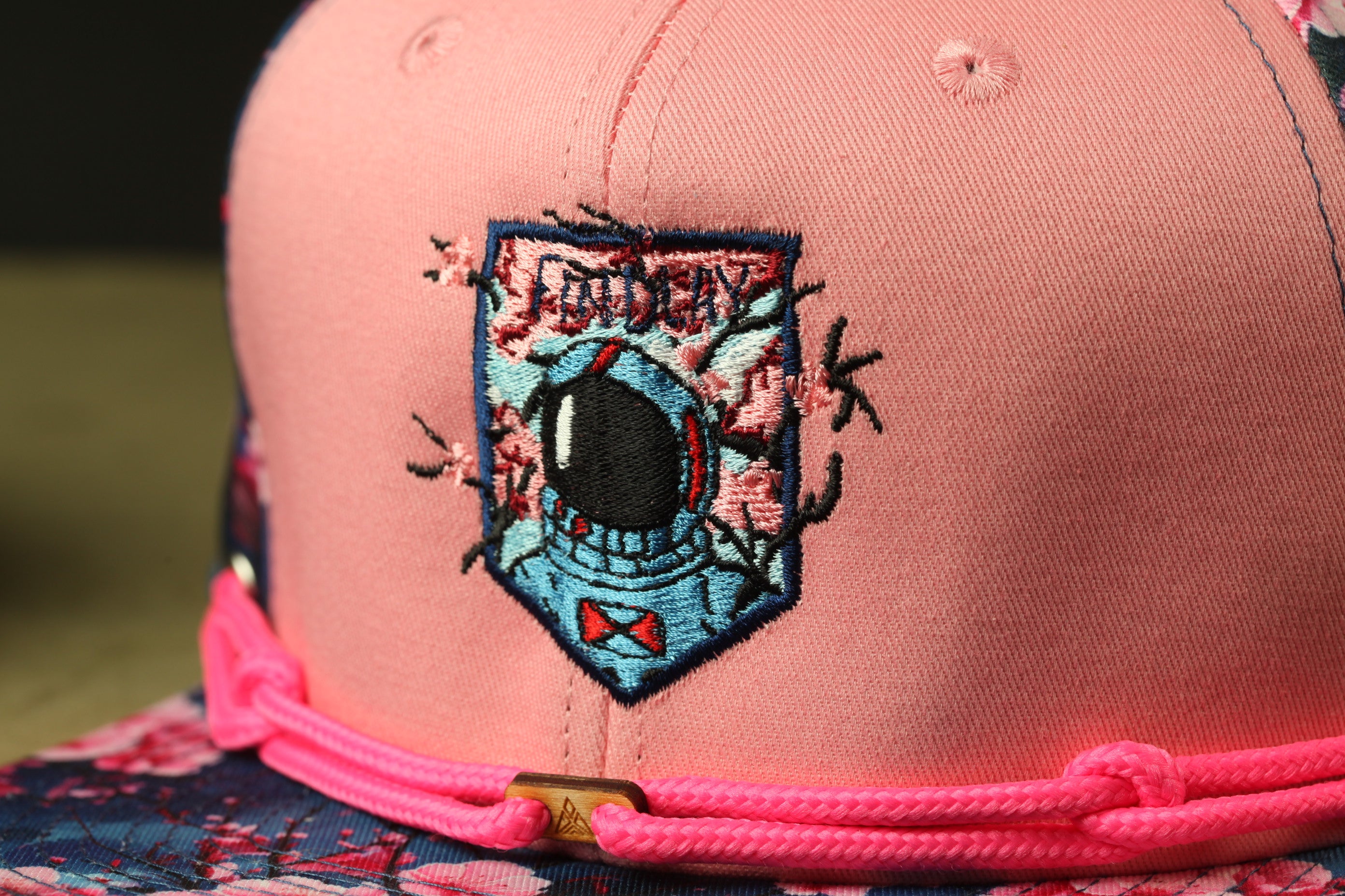 A close-up view of a pink baseball cap with a colorful embroidered patch on the front.