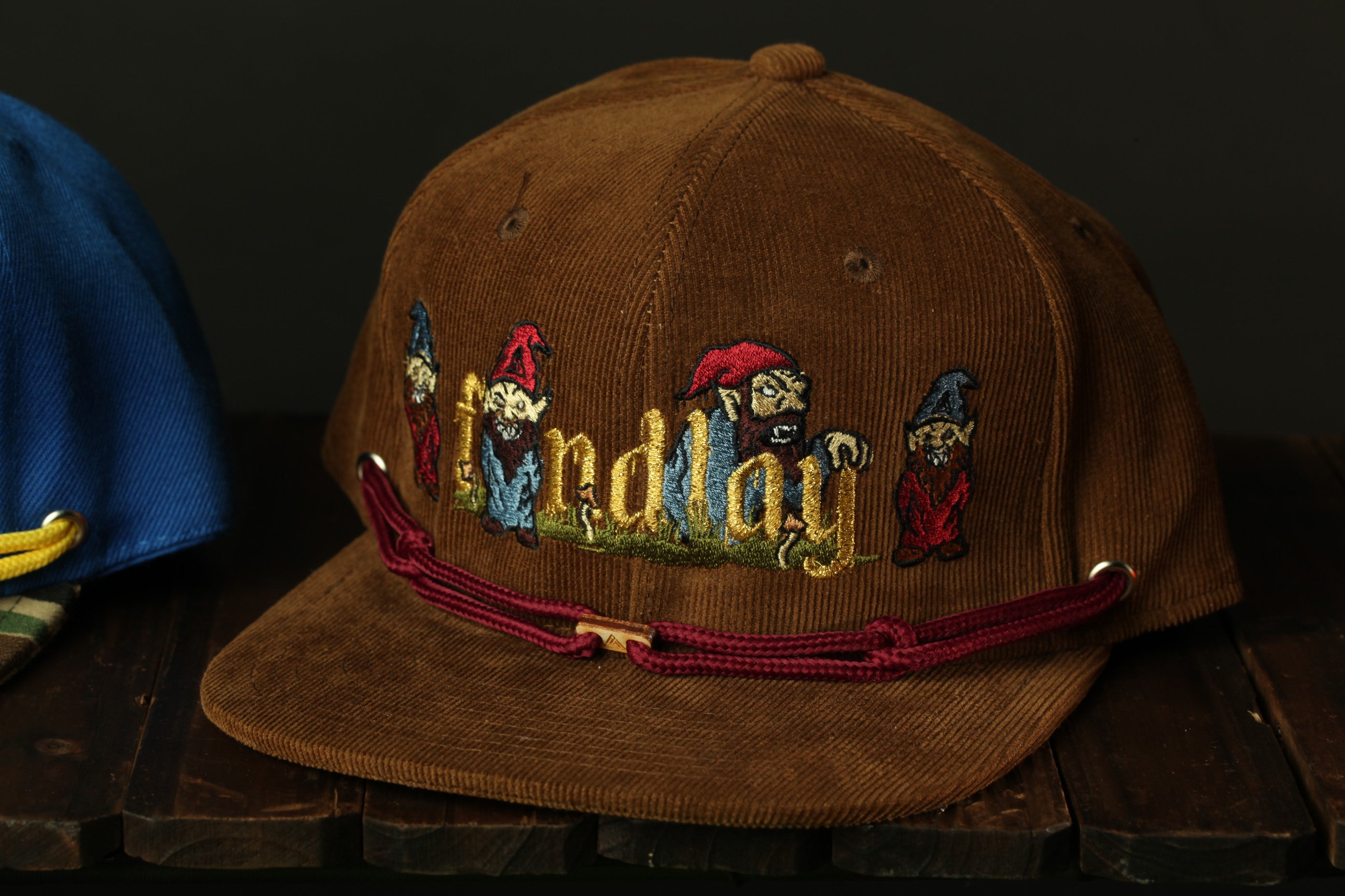 A brown baseball cap with a red string and a cartoonish design of dwarfs on it.