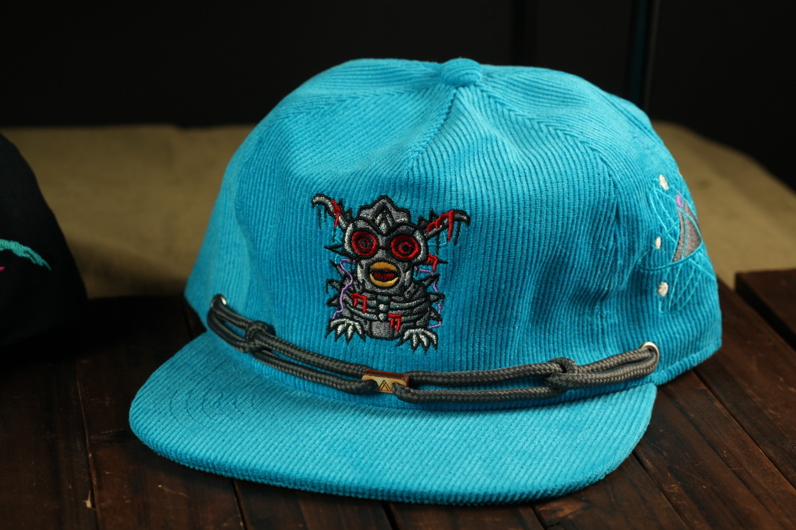 A blue baseball cap with a cartoon-like design on the front, featuring a red and black eye and a skull-like face.