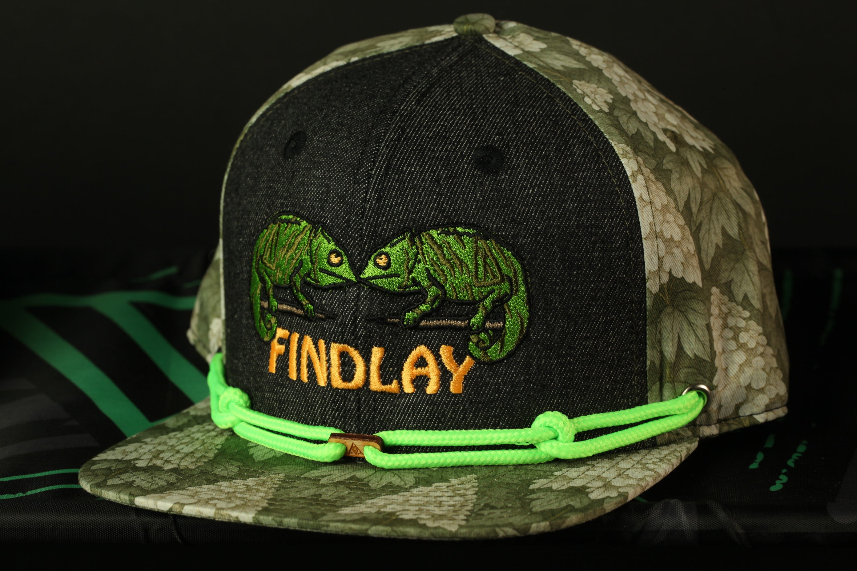 A camouflage baseball cap with a green rope and the word "FINDLAY" printed on it.