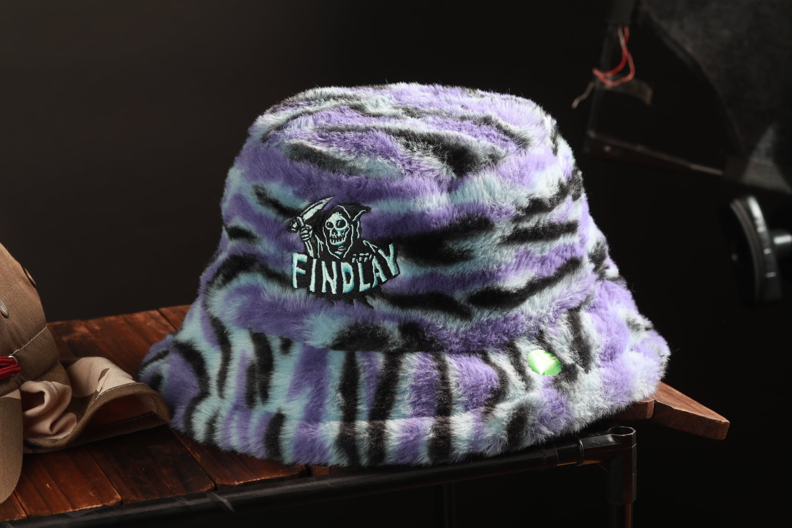 A purple and black zebra-striped bucket hat with a skull and crossbones design, sitting on a wooden surface.