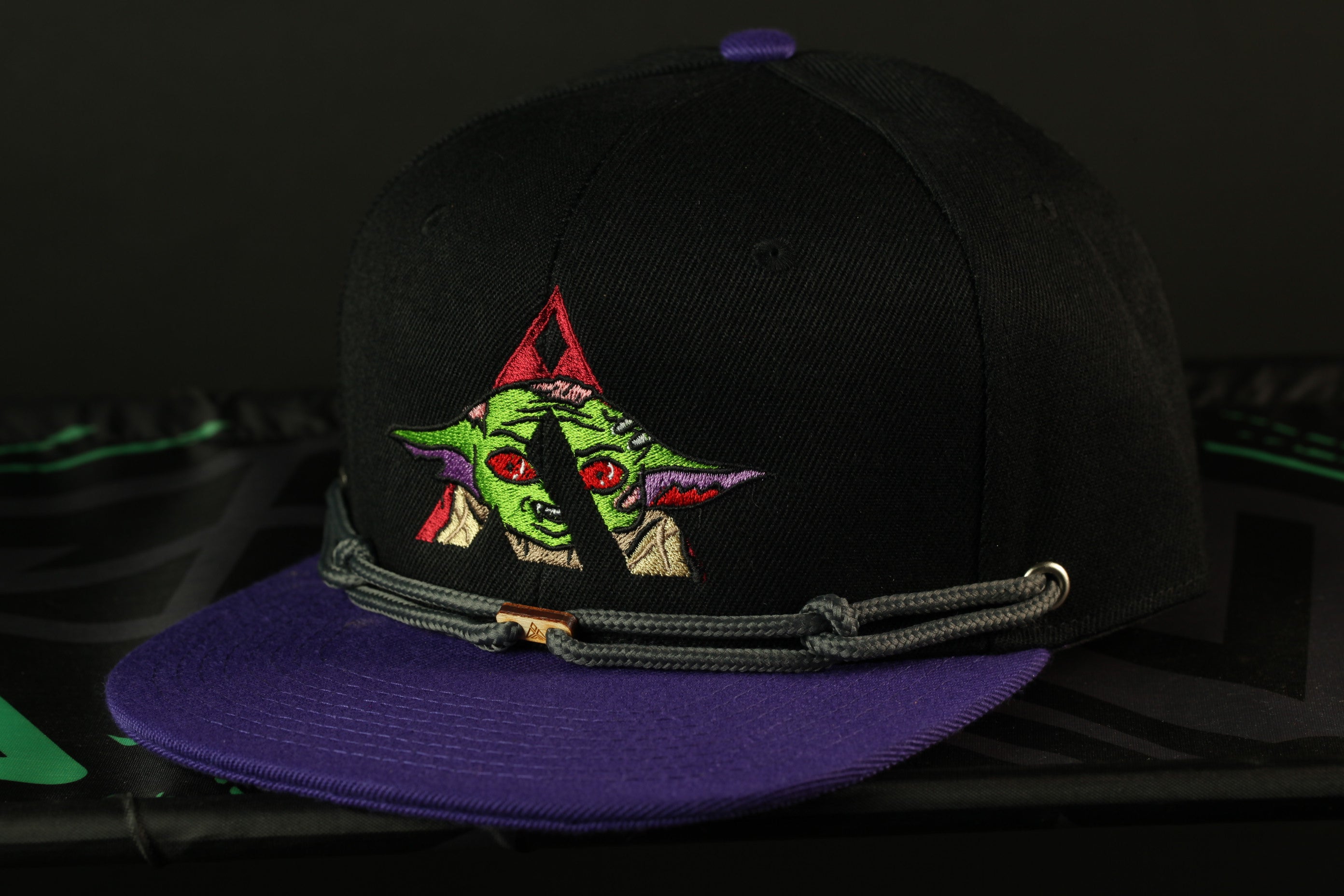 A black baseball cap with a purple brim and a colorful graphic of a character on the front.