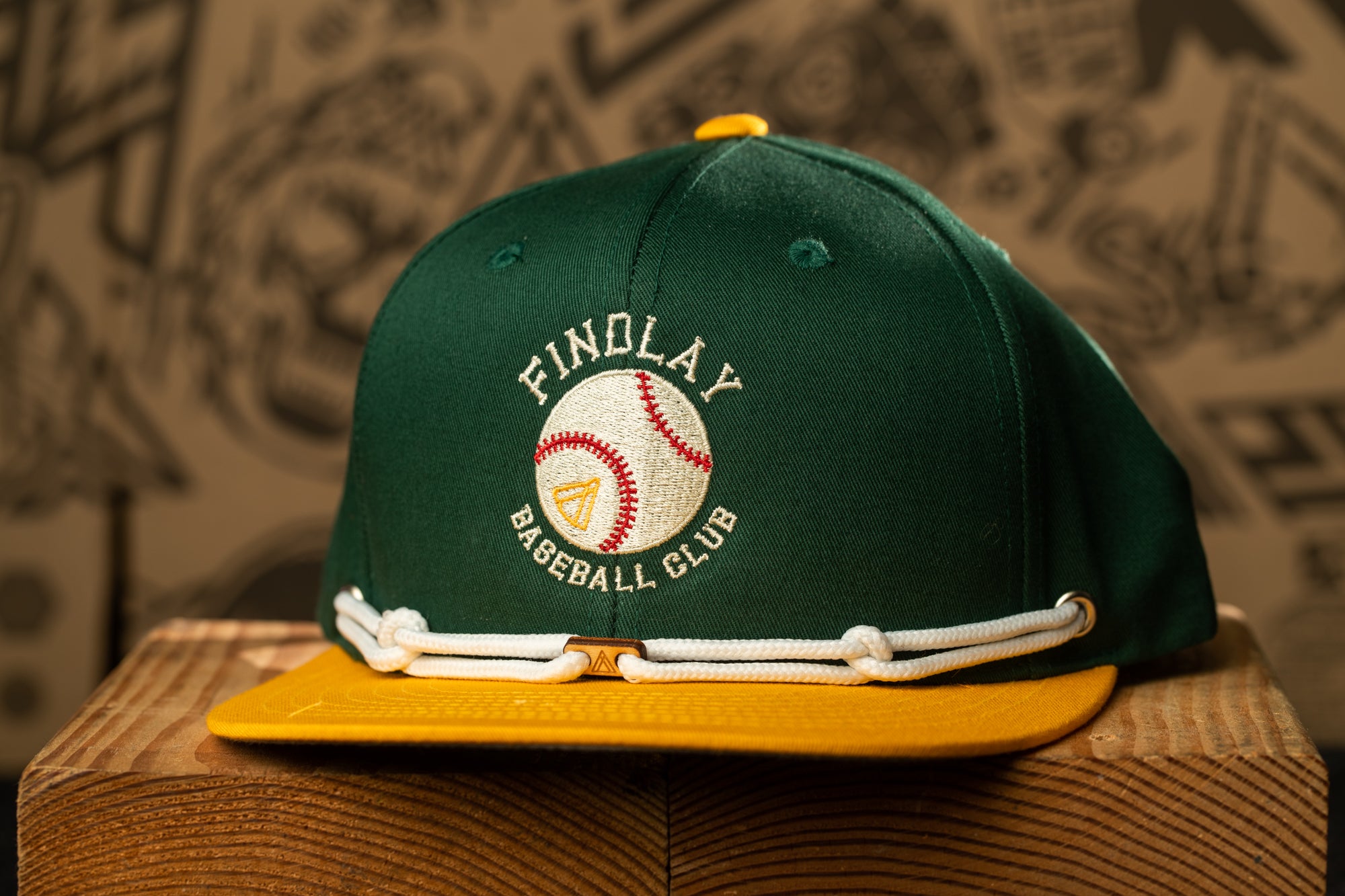 A green baseball cap with white stitching and a yellow brim, featuring the text "FINOLAY BASEBALL CLUB" on the front.