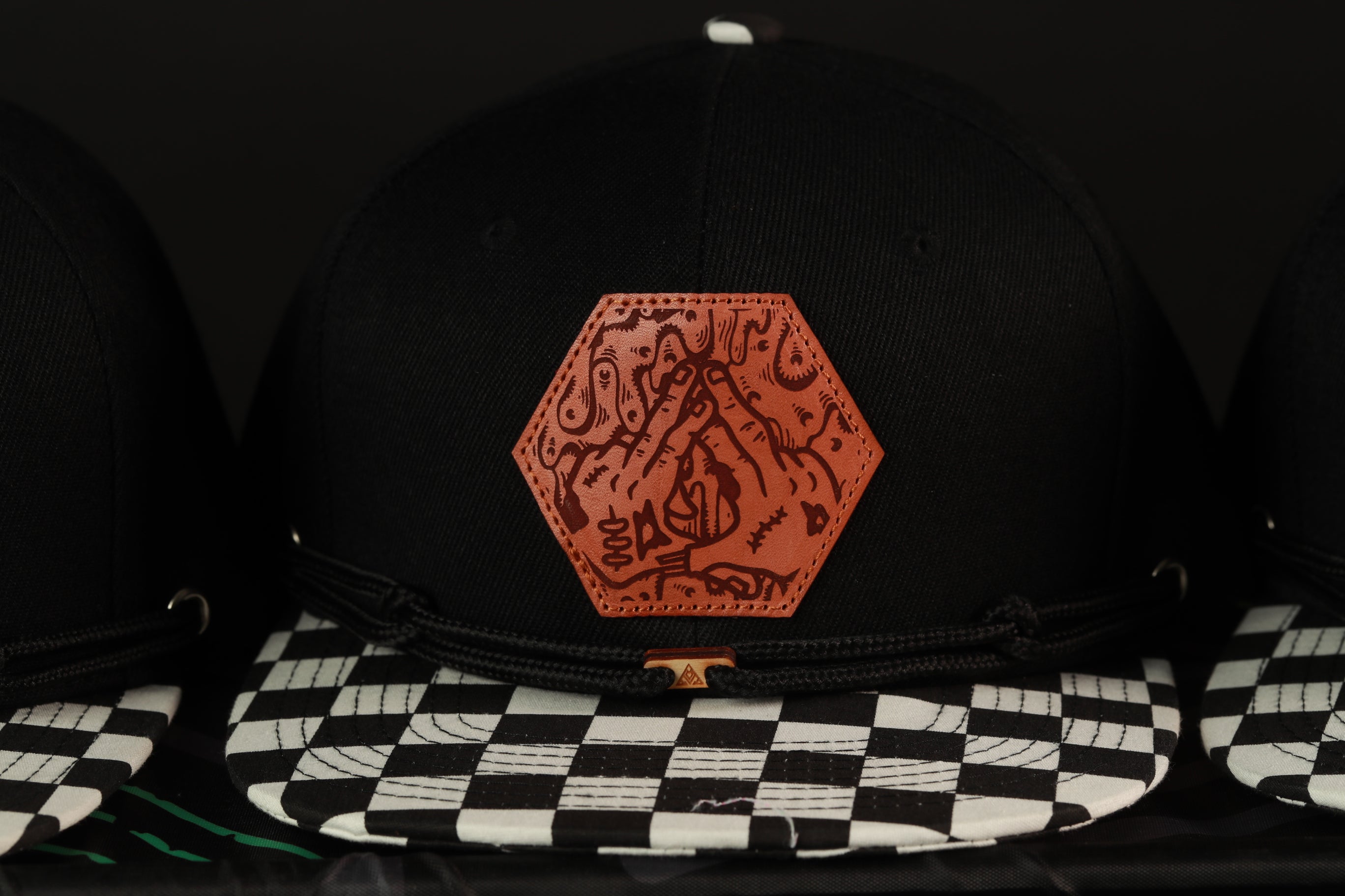 A close-up view of a black baseball cap with a distinctive orange patch featuring a hand-drawn design.