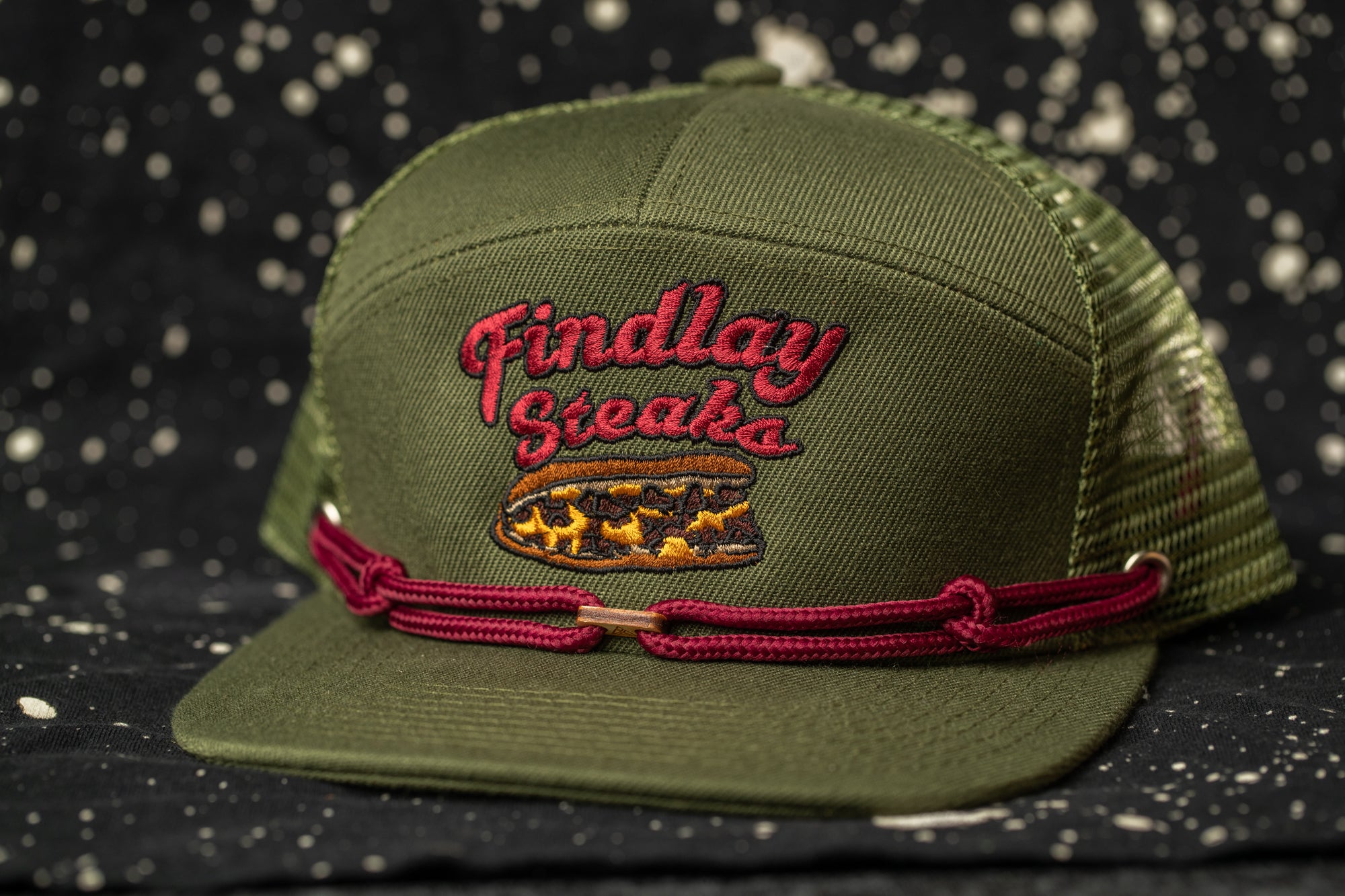 A green baseball cap with a red band and embroidered text on it.
