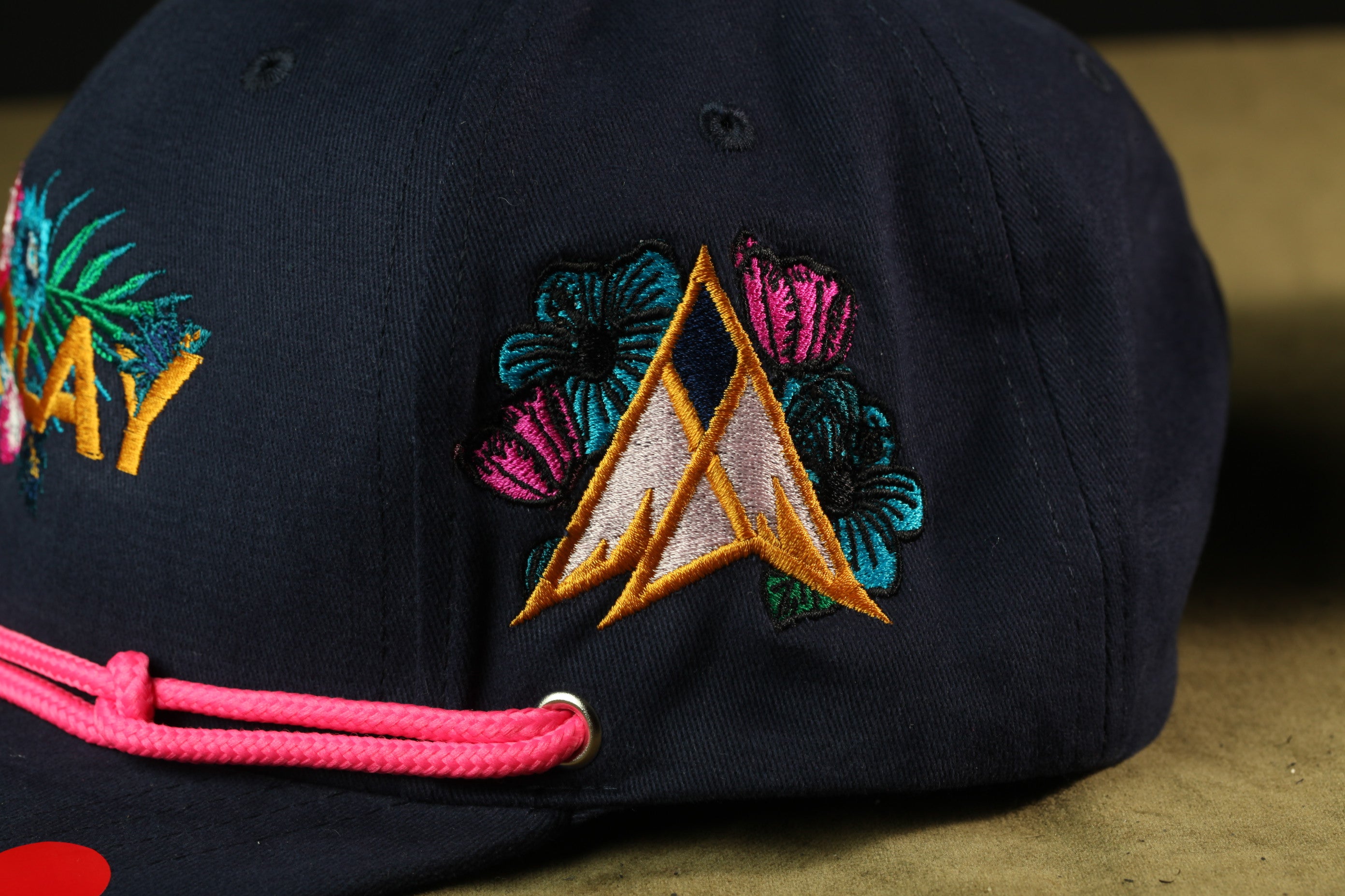 A close-up view of a dark-colored baseball cap with colorful floral embroidery and a pink string.