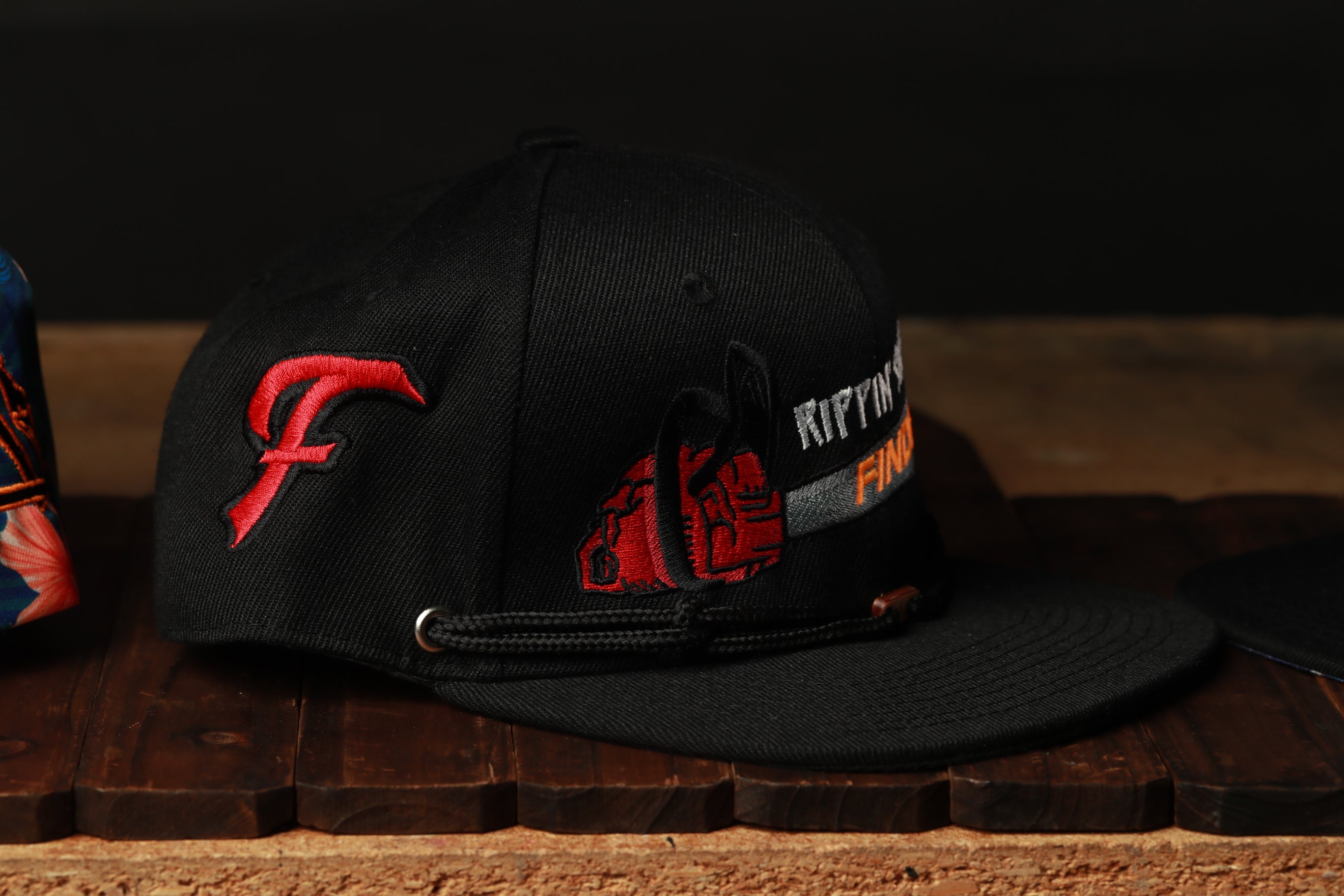 A black baseball cap with red and orange embroidered designs on it, placed on a wooden surface.