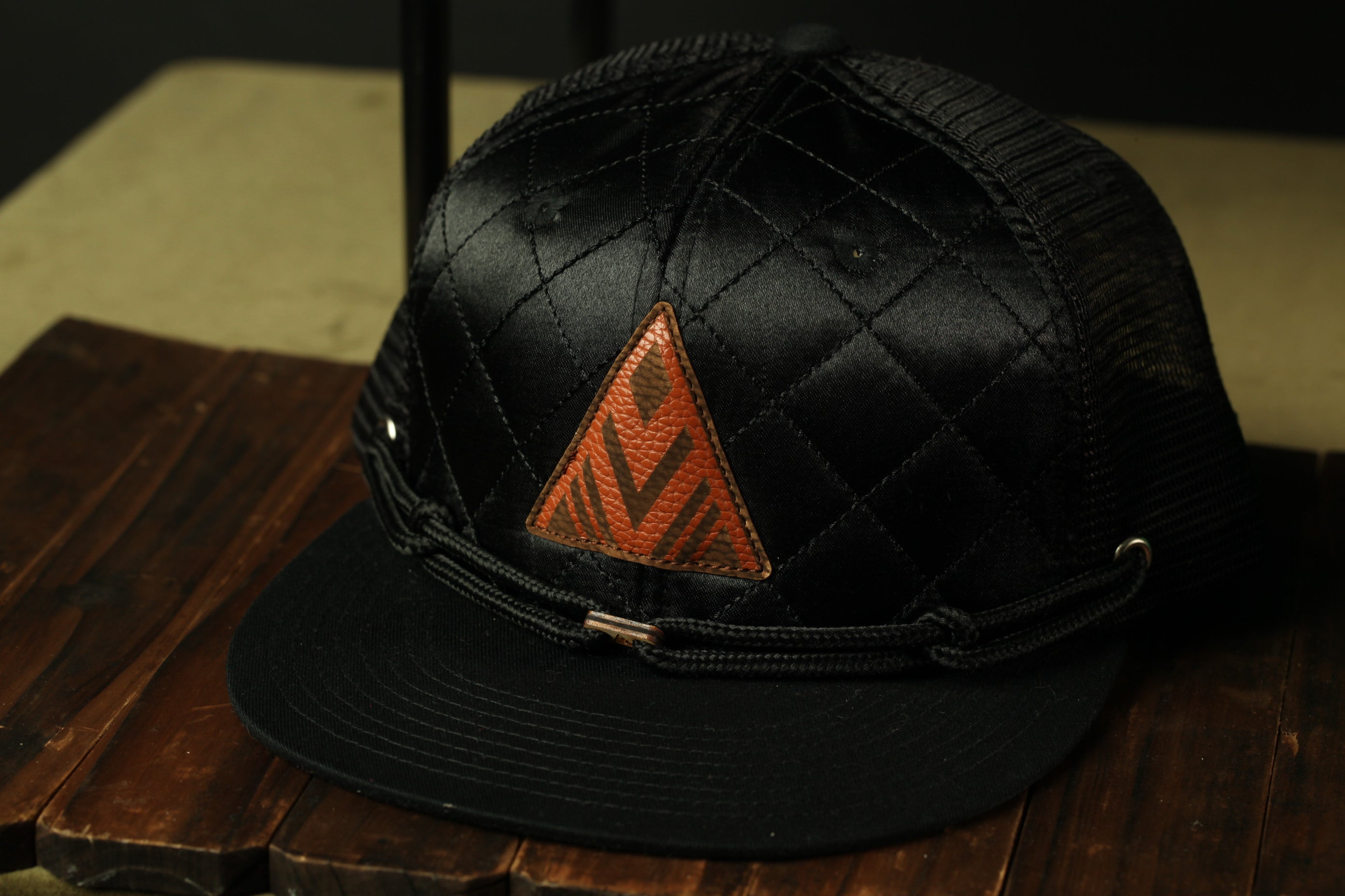 A black baseball cap with a distinctive orange triangle logo on the front, resting on a wooden surface.