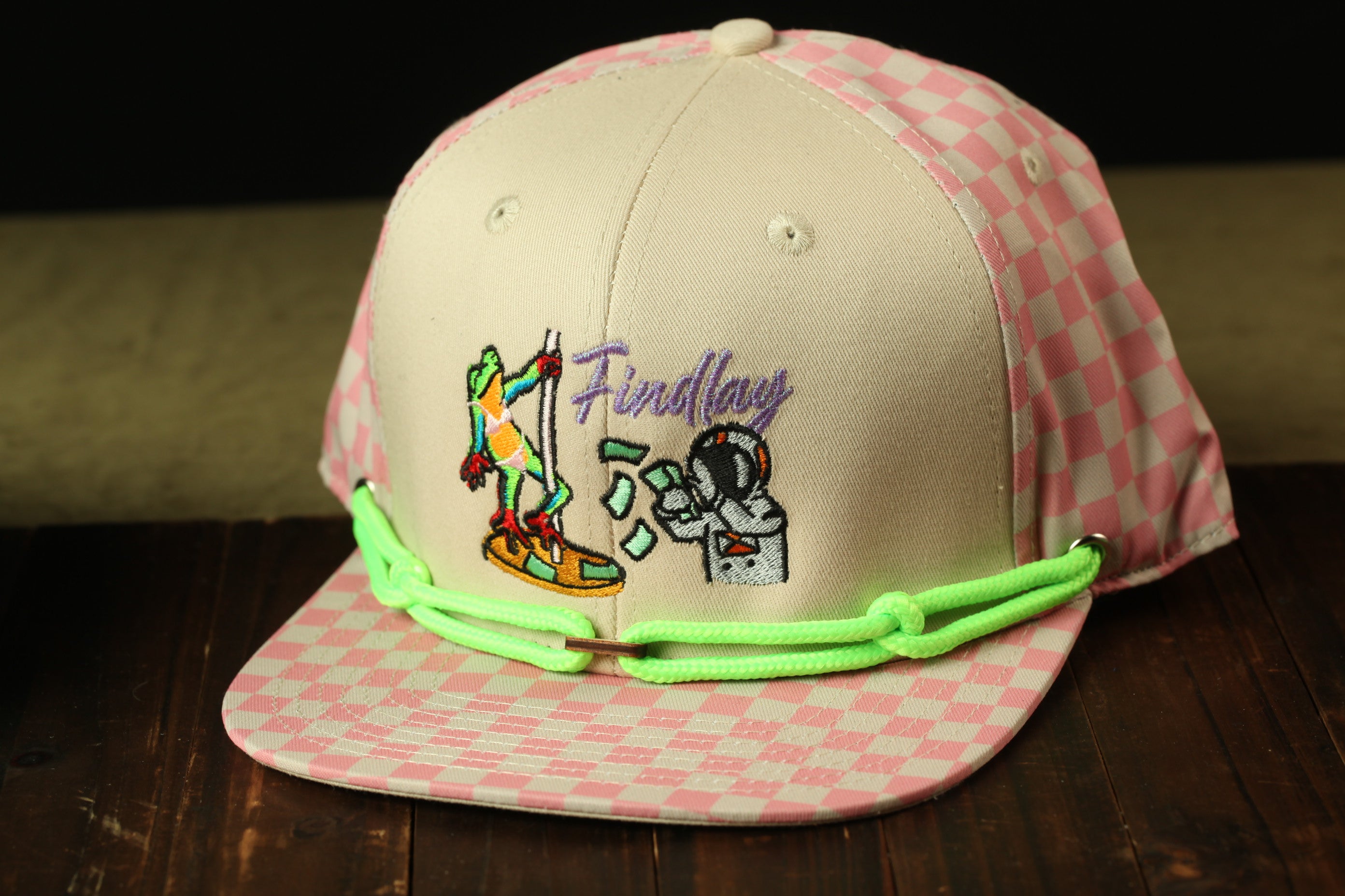 A pink and white baseball cap with a cartoon character and text on it, sitting on a wooden surface.