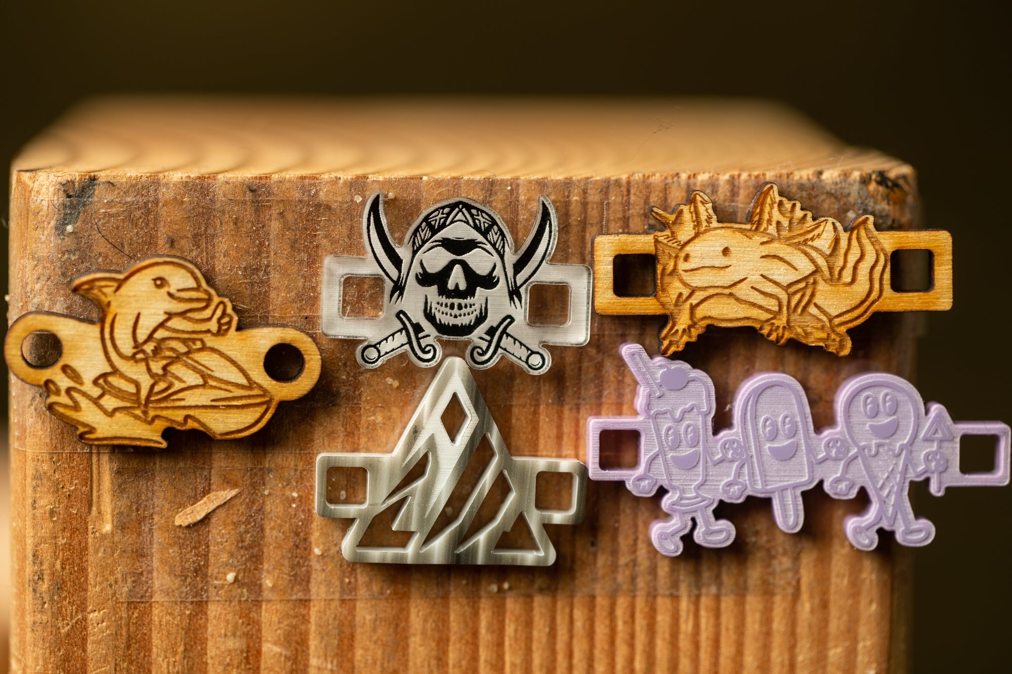a collection of five unique objects, including a wooden shark, a pirate skull, a cartoon character, a cartoon fish, and a cartoon character, all displayed on a wooden surface.