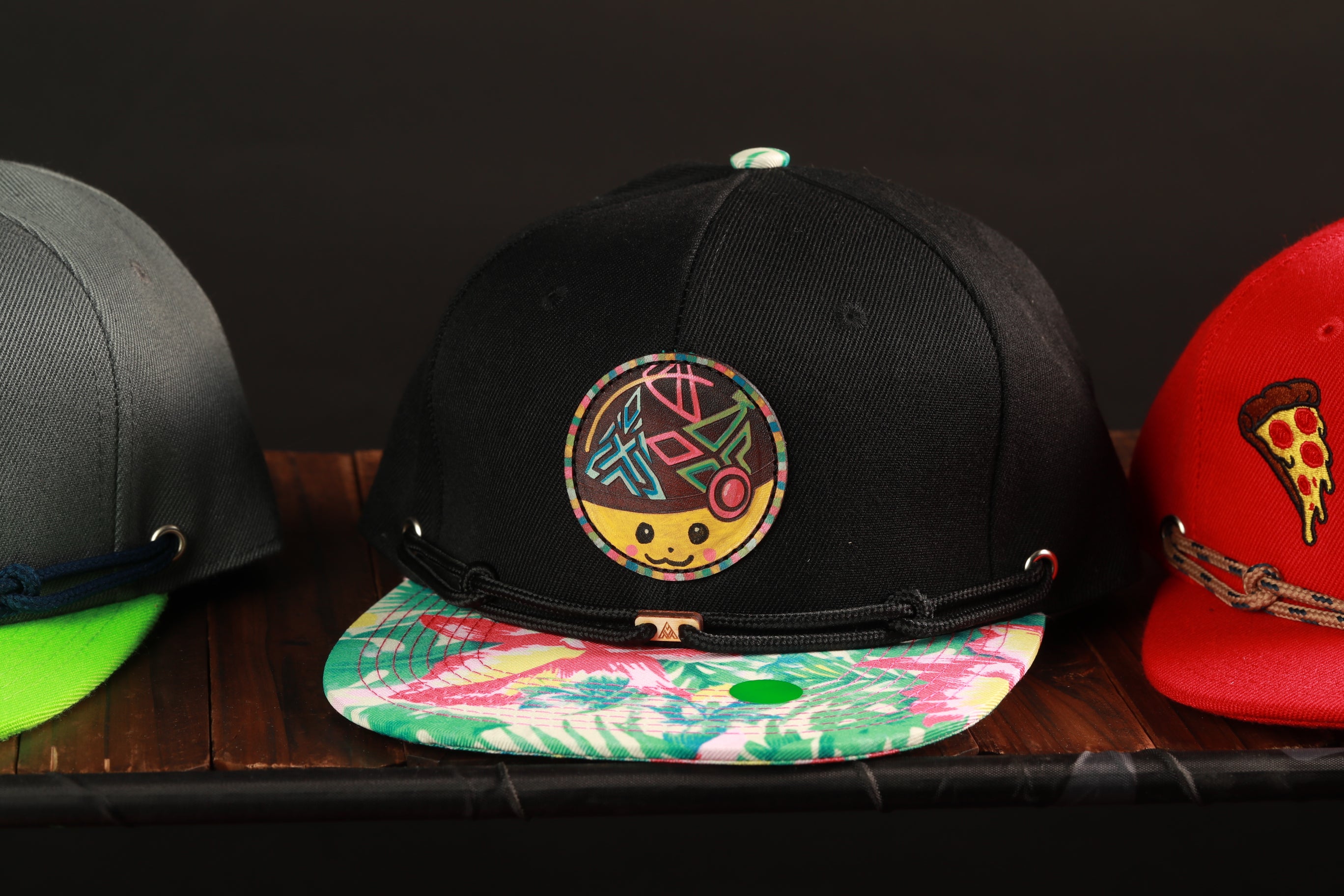 Three colorful baseball caps are displayed on a wooden surface, with one featuring a unique circular design.