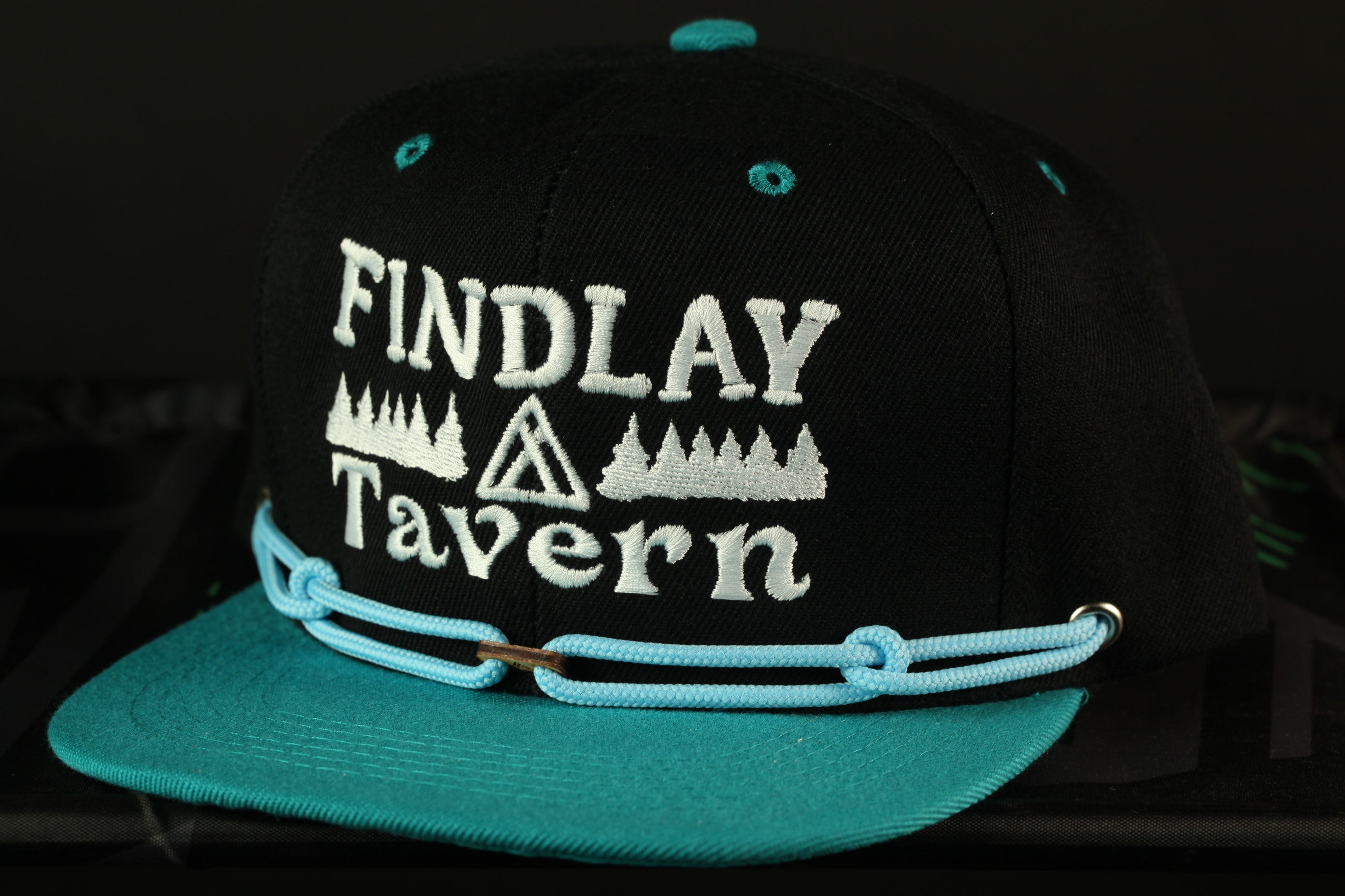 A black baseball cap with teal trim, featuring the text "FINDLAY TAVERN" embroidered on it.