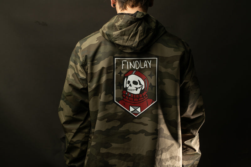 A person wearing a camouflage jacket with a skull and crossbones design on the back.