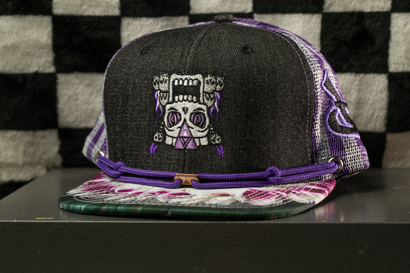 A black baseball cap with a skull design and purple accents, placed on a black surface against a checkered background.