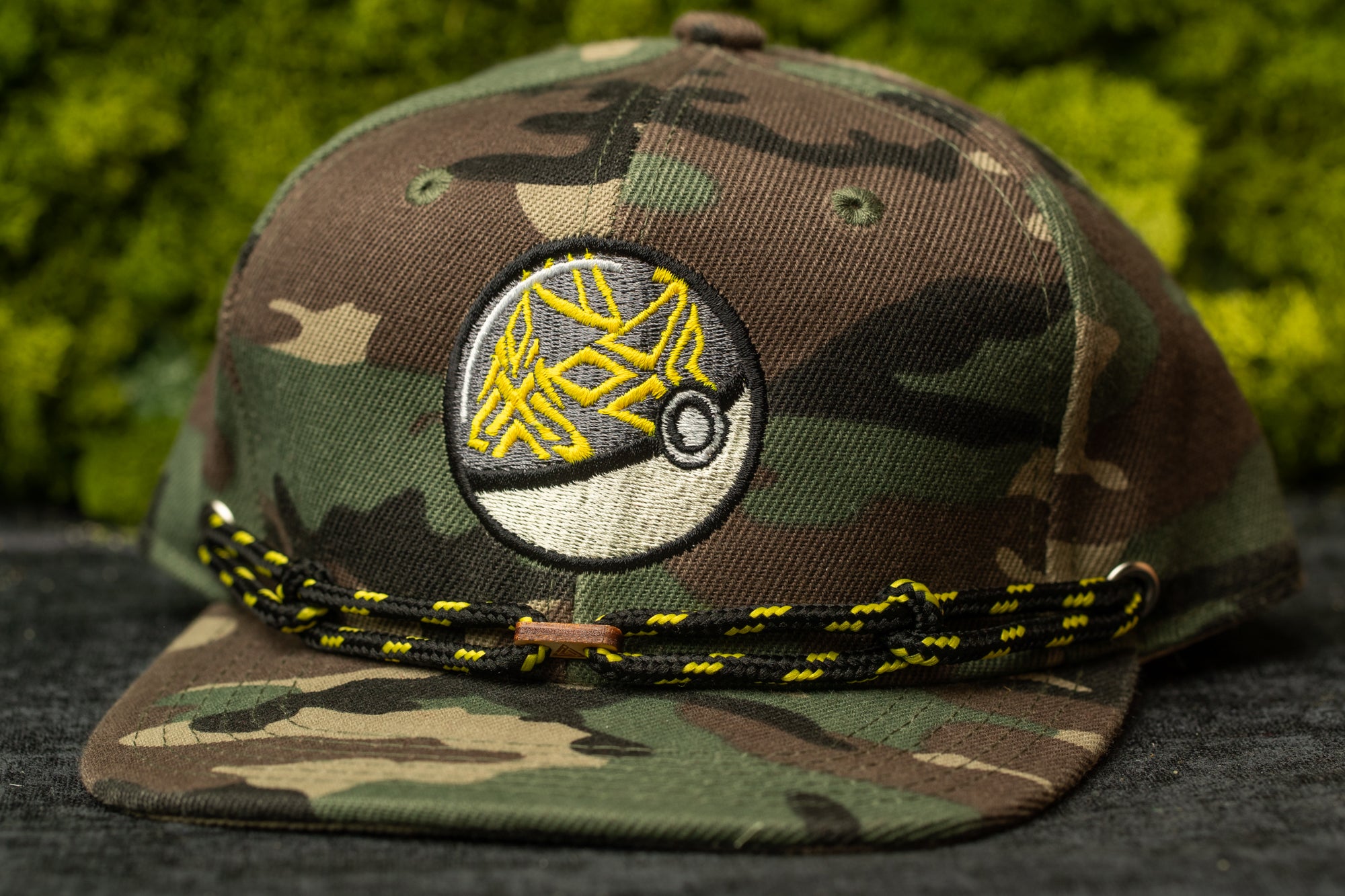 A camouflage baseball cap with a yellow and black braided strap.