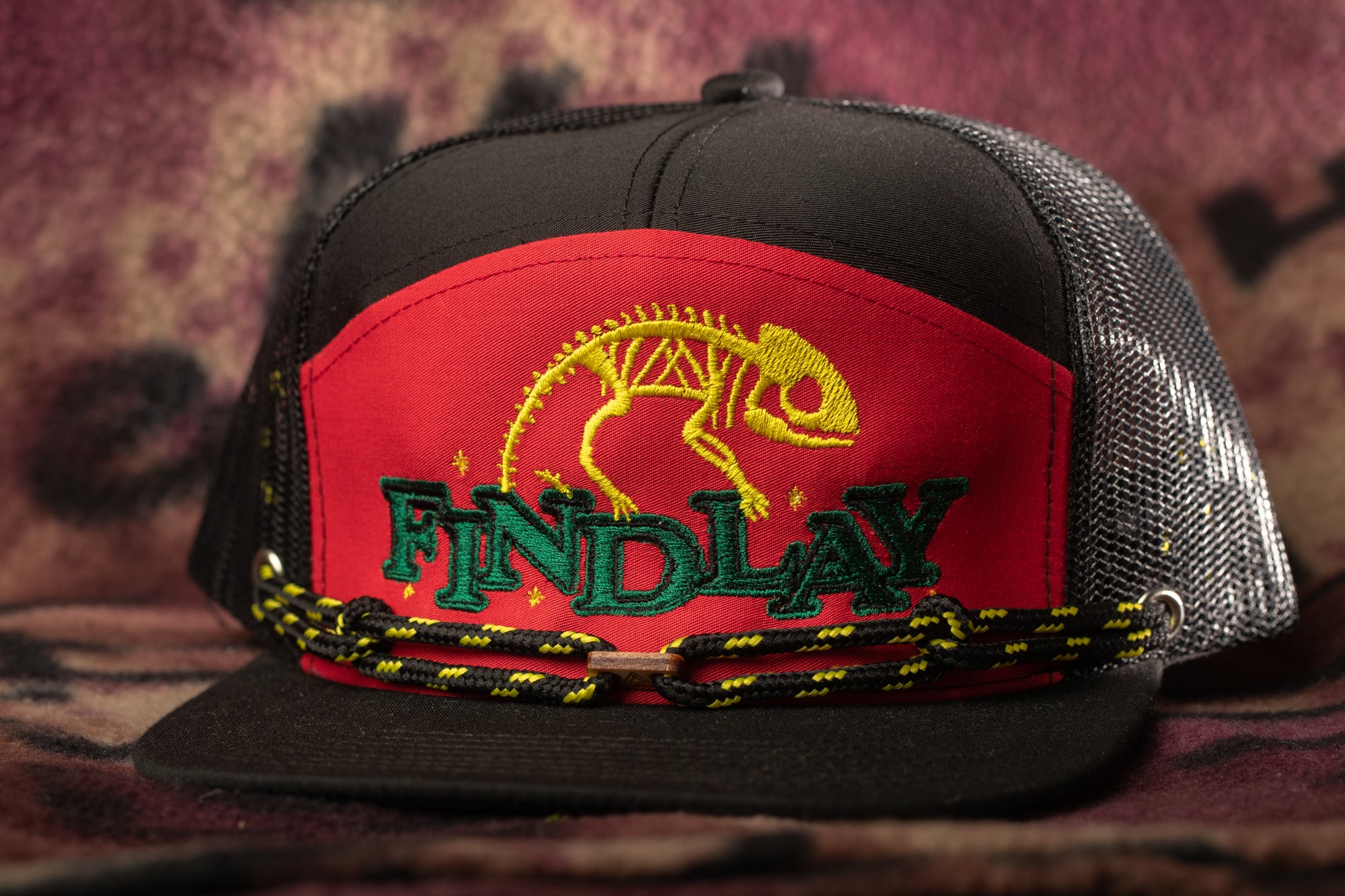 A black baseball cap with a red and green design, featuring a chameleon and the word "FIND LAY" printed on it.